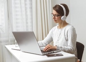 woman typing on laptop with headphones in