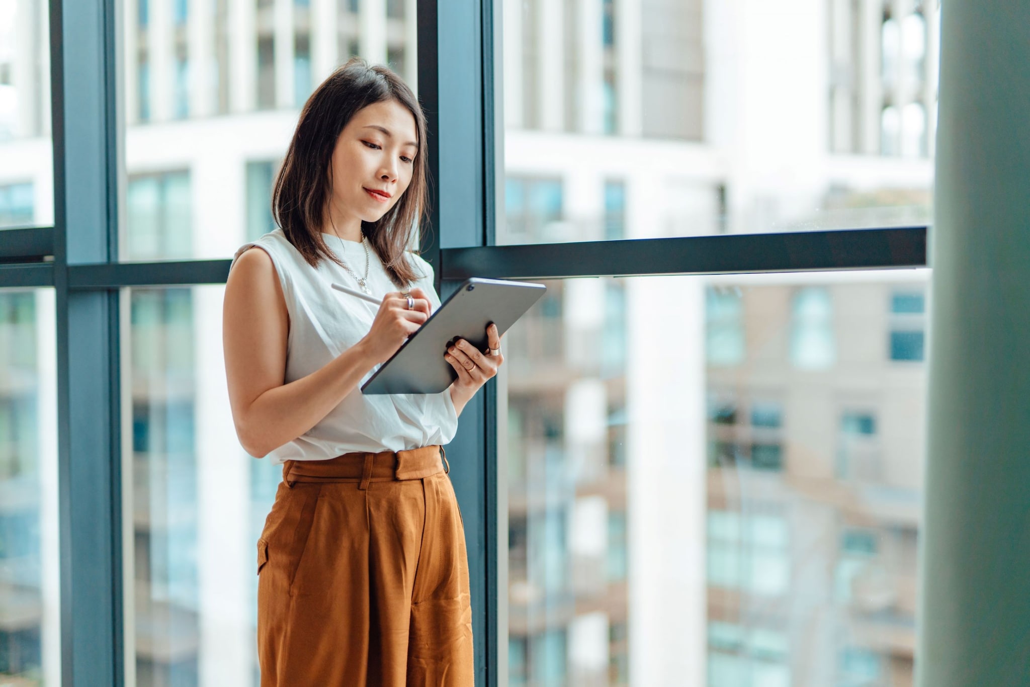 Woman standing by a window working on a computer tablet