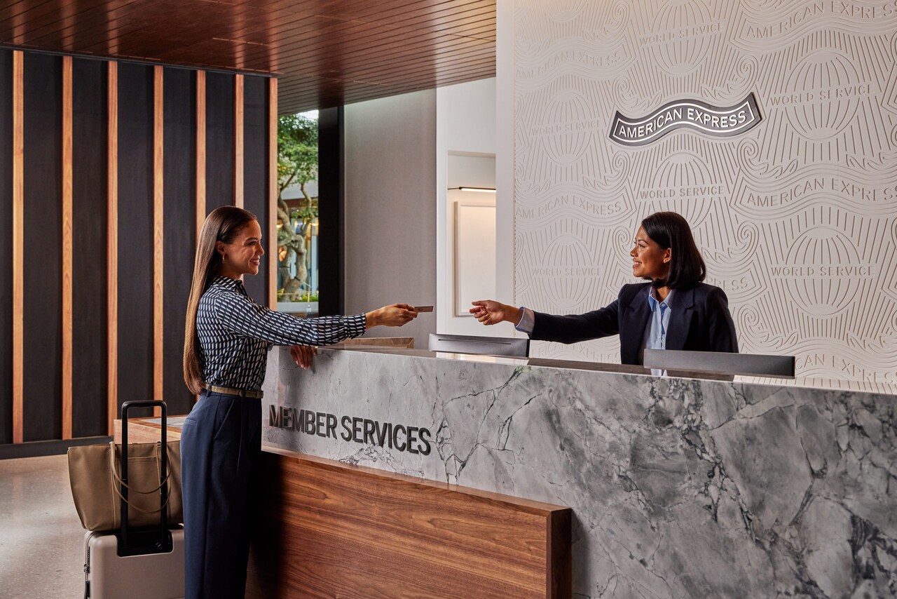 Eine Frau reicht einer anderen Frau an der Rezeption ihre goldene AMEX Karte.