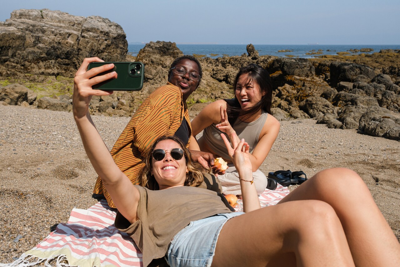 Drei Frauen machen Selfie am Strand.