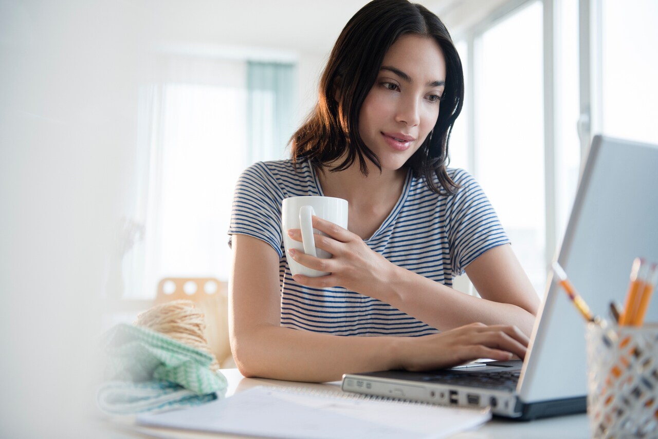 Eine Frau sitzt an einem Tisch mit einem Laptop und einer Tasse Kaffee.