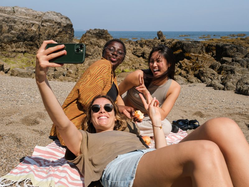 Drei Frauen machen Selfie am Strand.