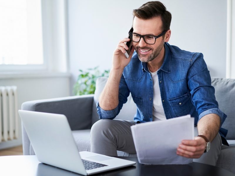 Ein Mann sitzt auf einem Sofa mit einem Laptop und Papieren.