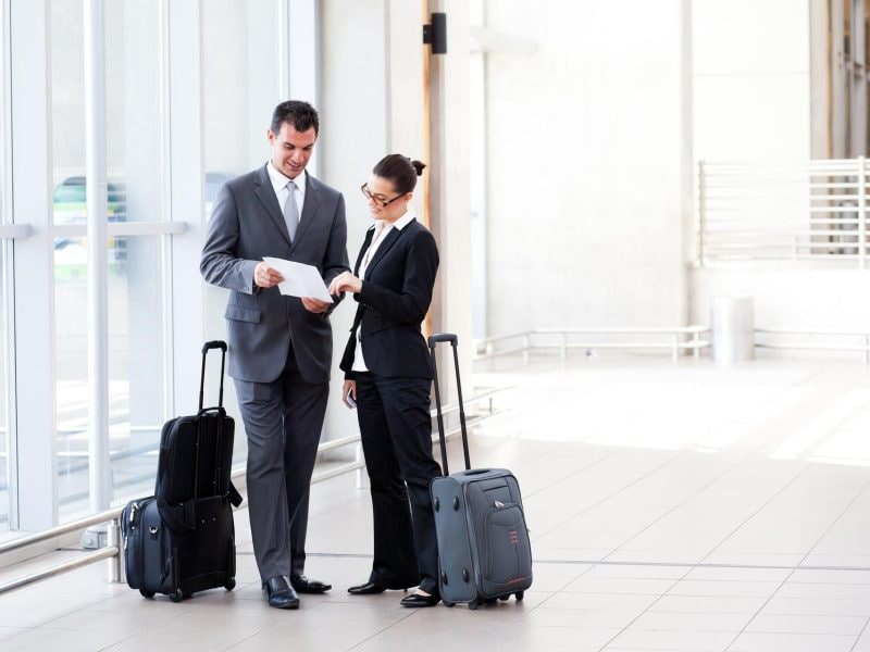 Zwei Mitarbeiter in Anzügen und Koffer besprechen ein Dokument am Flughafen