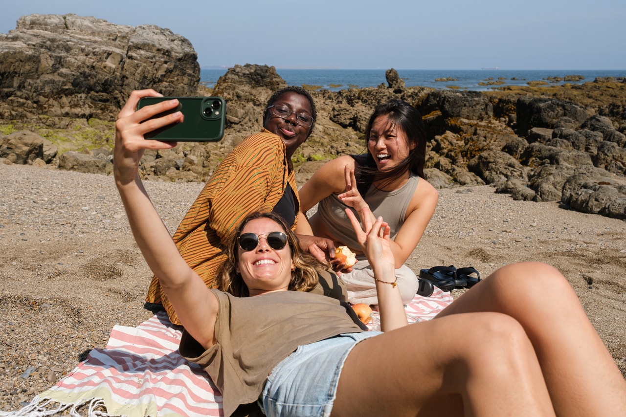 Drei Frauen machen Selfie am Strand.