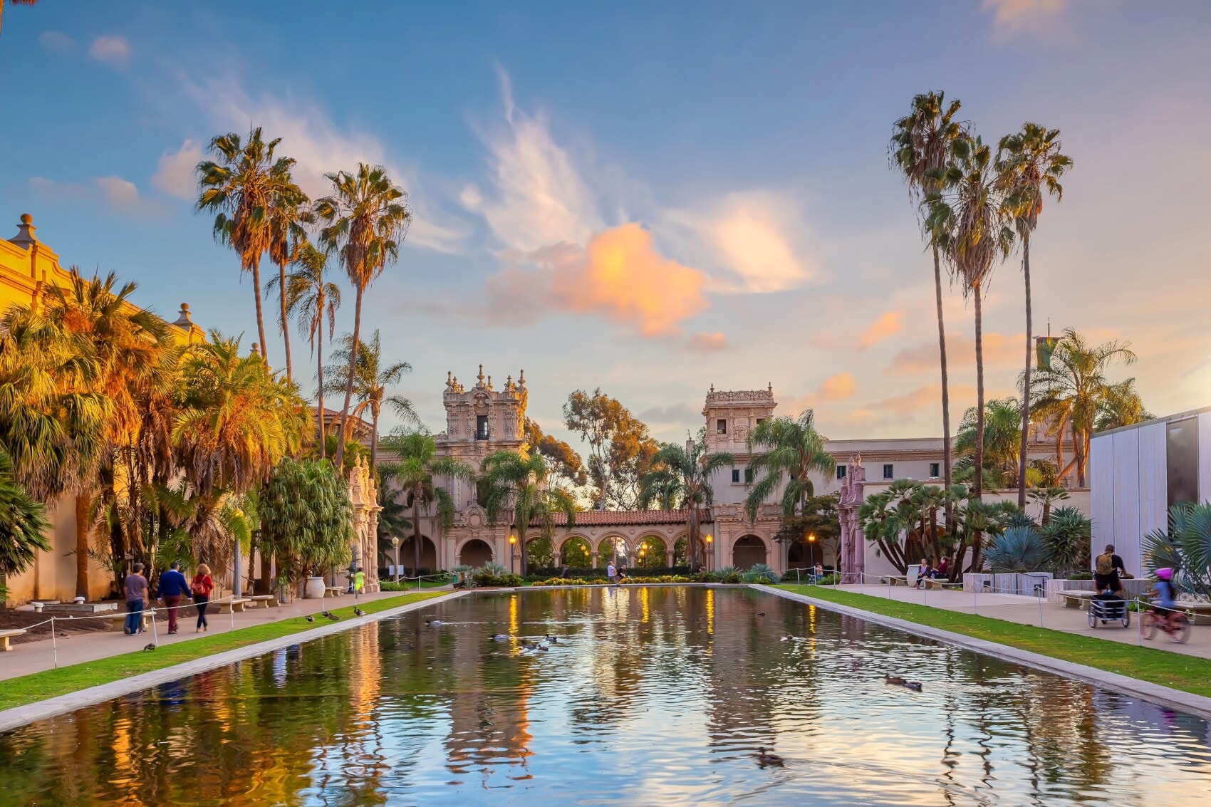 Blick auf einen angelegten Teich in der Abendsonne mit Palmen drumherum und einem Bauwerk im Hintergrund Blick auf einen angelegten Teich in der Abendsonne mit Palmen drumherum und einem Bauwerk im Hintergrund