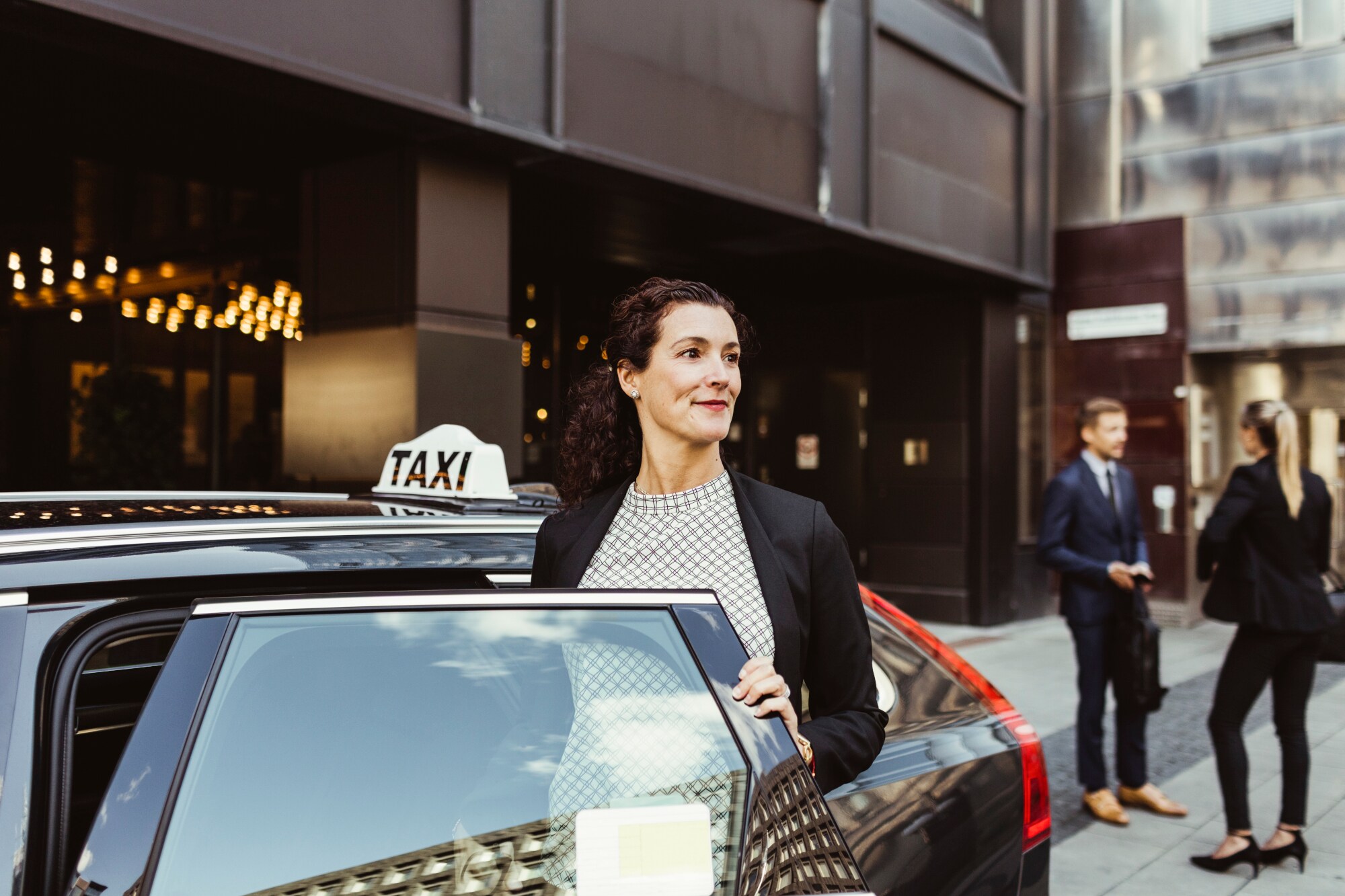 Eine Frau steigt aus einem schwarzen Taxi vor einem Hotel.