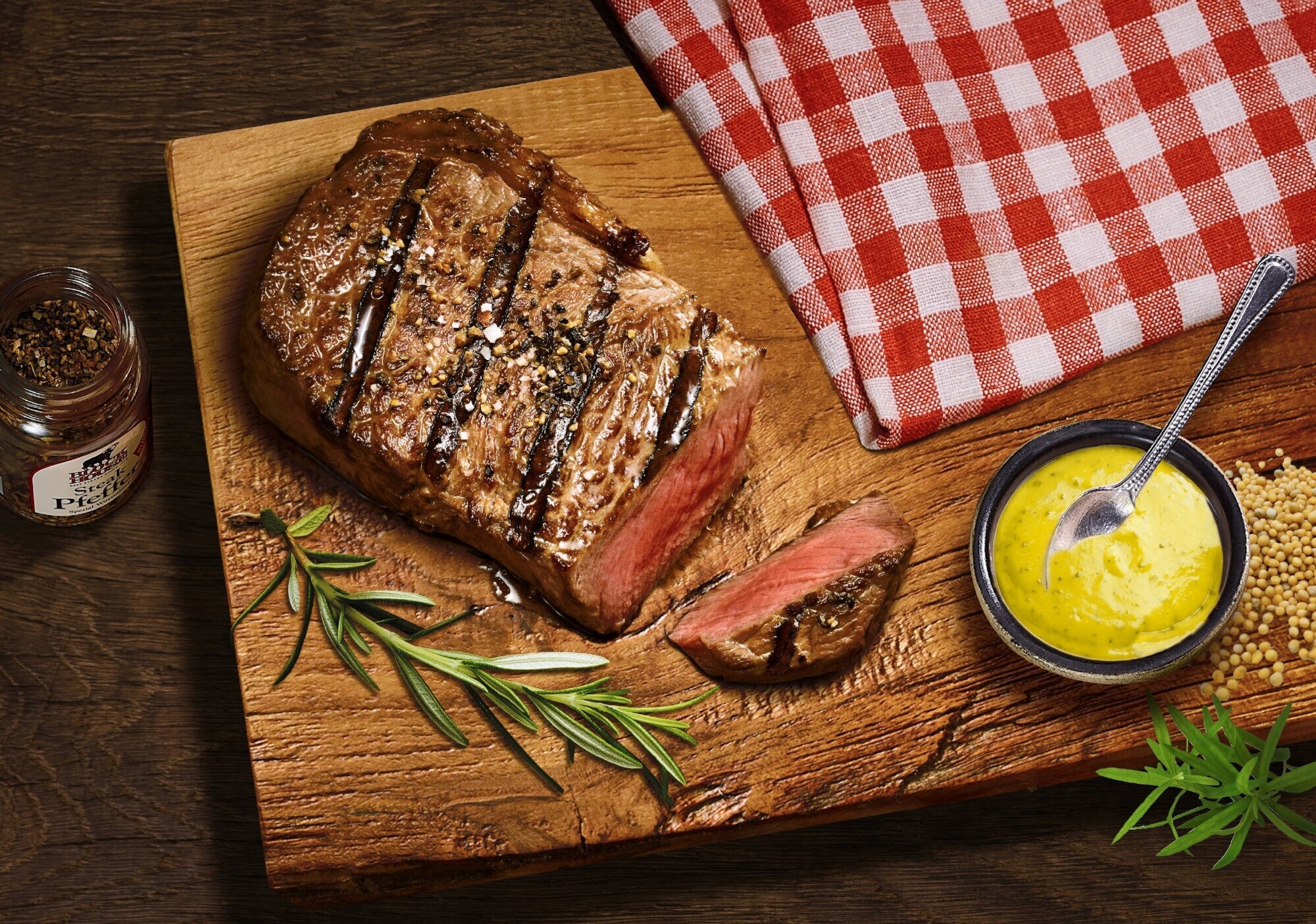Aufsicht eines gebratenen, angeschnittenen Steaks auf einem Brett neben einer Schale mit Senf.