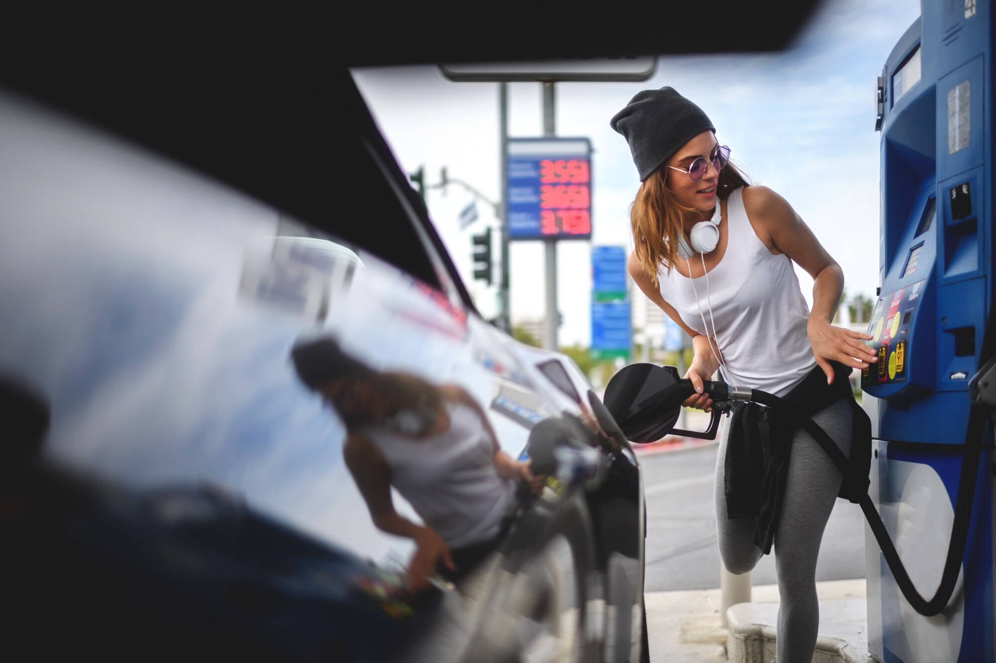 Eine junge Frau in Sportkleidung beim Tanken an einer Zapfsäule