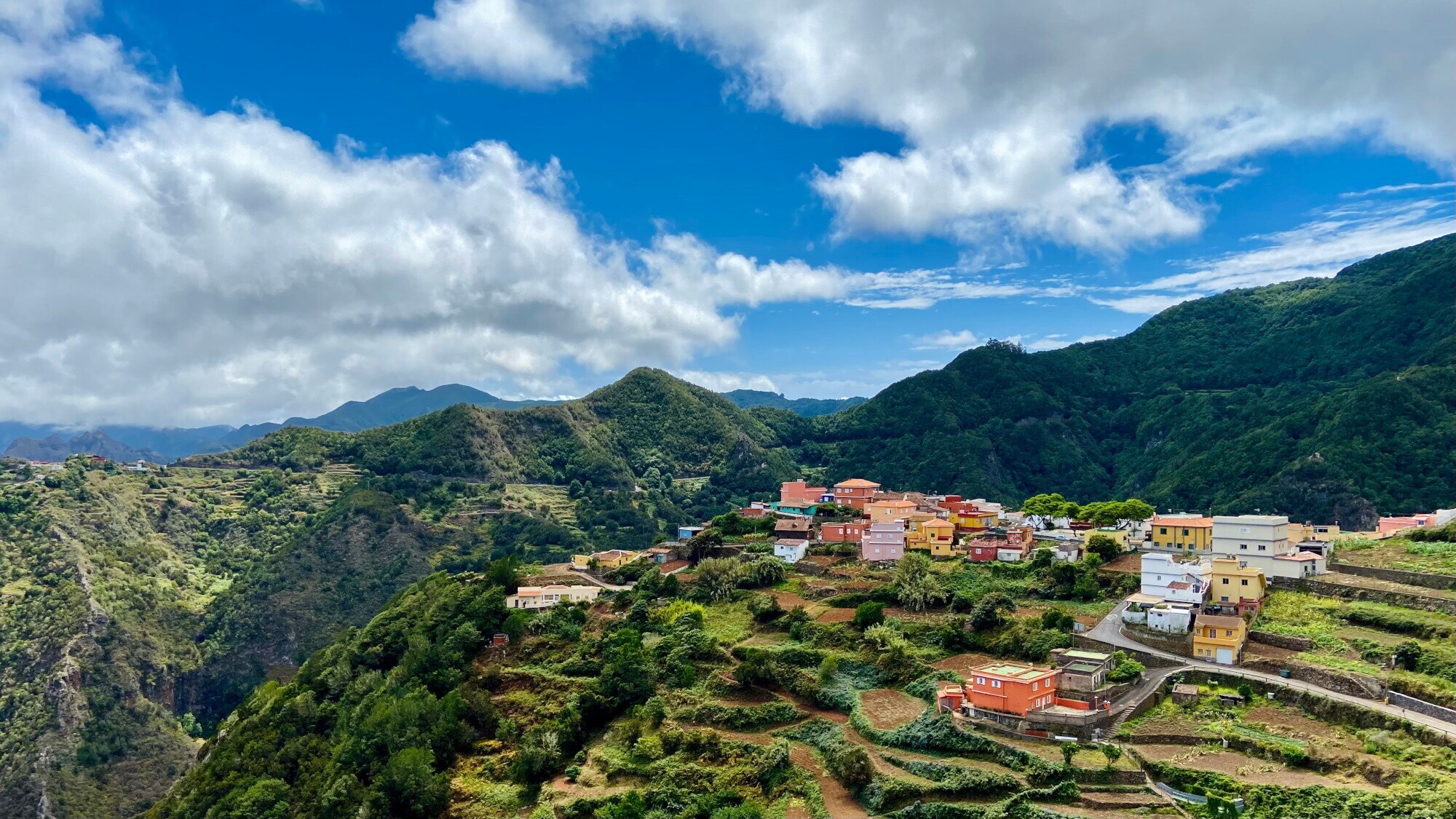 Ein kleines Bergdorf mit bunten Häusern auf einem Plateau mit landwirtschaftlichem Terrassenbau inmitten einer grünen Berglandschaft