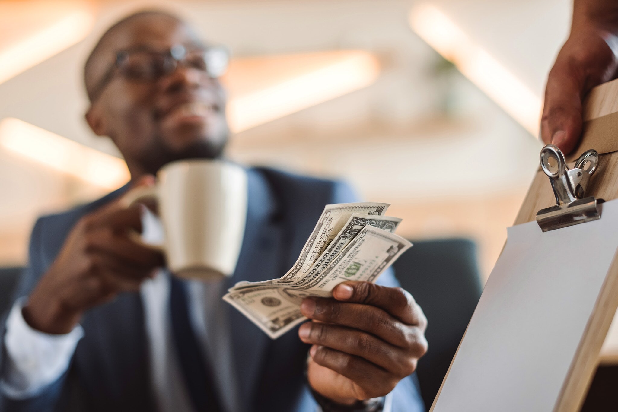 Nahaufnahme von US-Dollar-Scheinen in der Hand eines Geschäftsmannes beim Bezahlen eines Kaffees. Nahaufnahme von US-Dollar-Scheinen in der Hand eines Geschäftsmannes beim Bezahlen eines Kaffees.