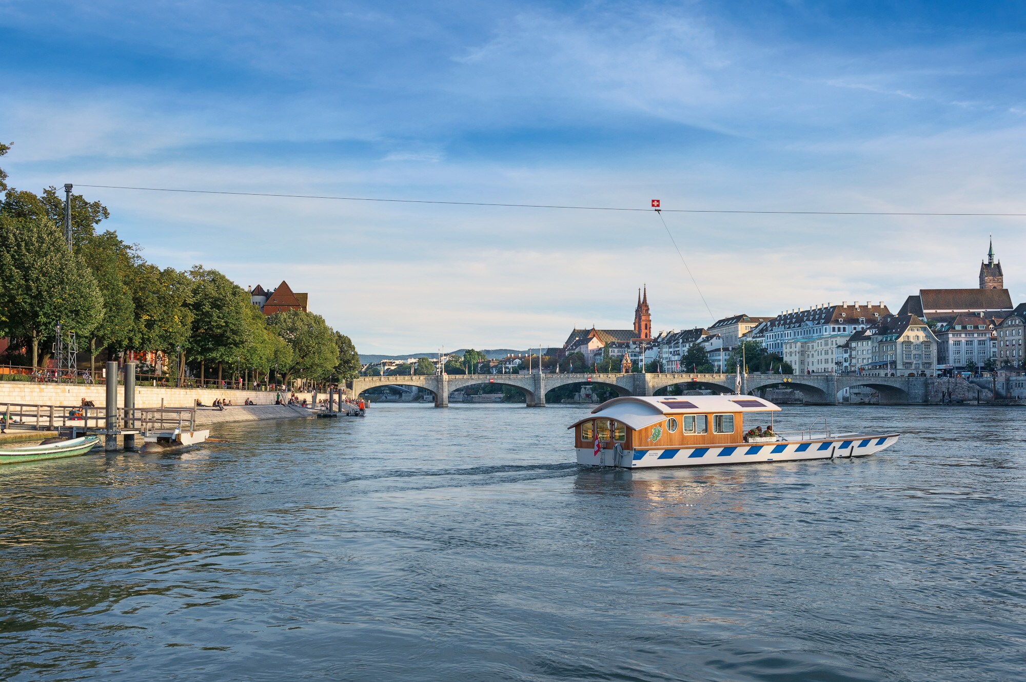 Eine kleine Fähre fährt an einem Seil entlang über den Rhein, im Hintergrund die Basler Altstadt. Eine kleine Fähre fährt an einem Seil entlang über den Rhein, im Hintergrund die Basler Altstadt.