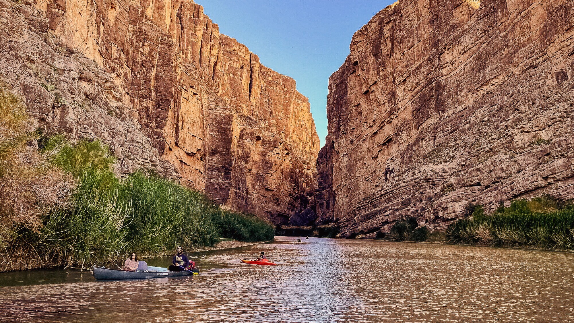 Personen in Kayaks auf einem Fluss in einem Canyon mit rötlichen Felsen.