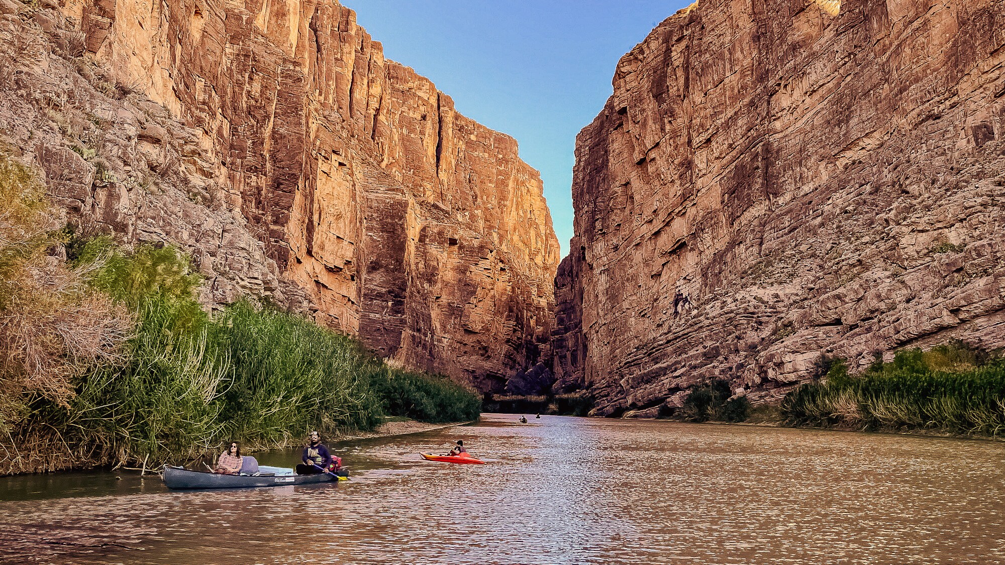 Personen in Kayaks auf einem Fluss in einem Canyon mit rötlichen Felsen. Personen in Kayaks auf einem Fluss in einem Canyon mit rötlichen Felsen.