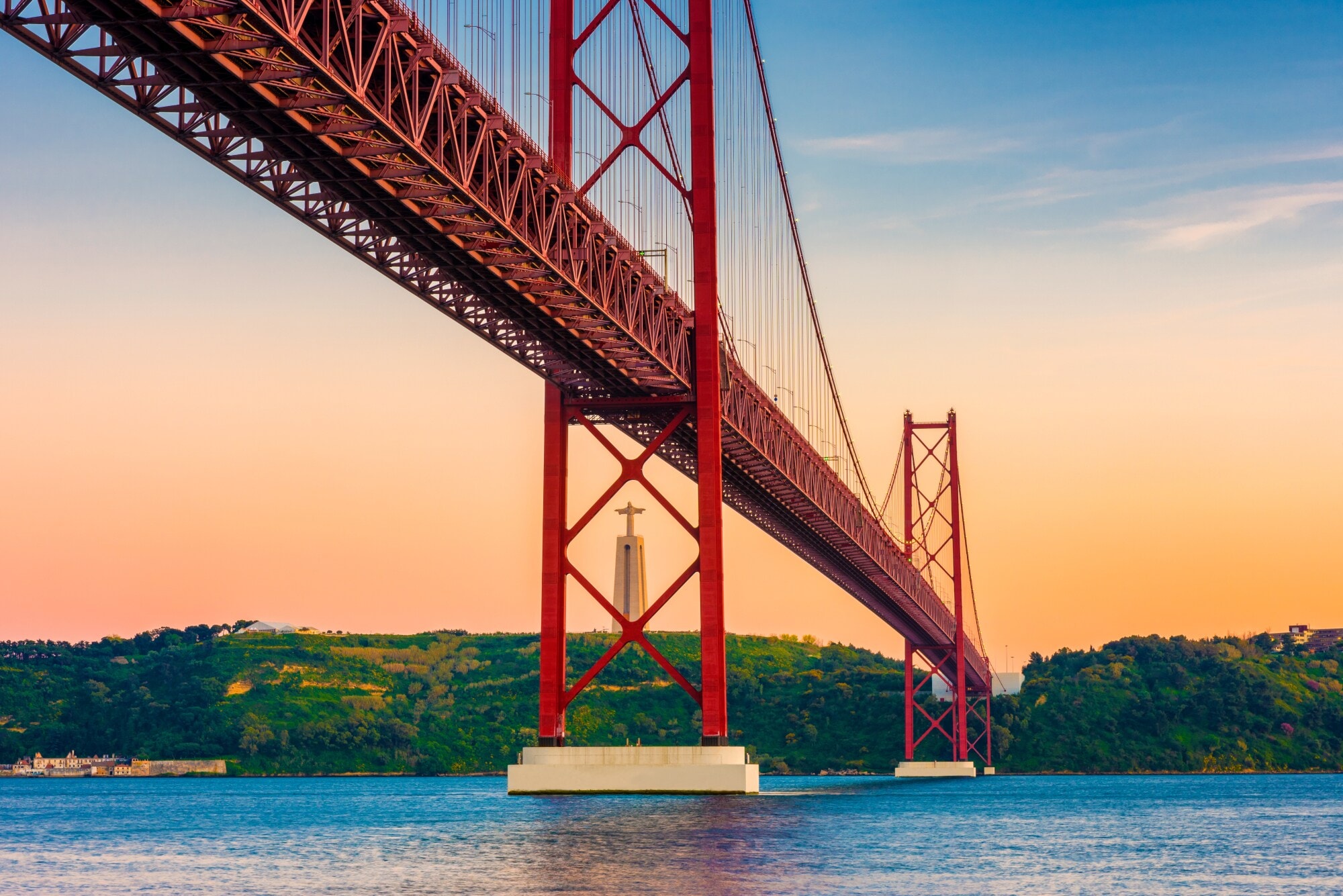 Rote Hängebrücke aus Stahl über einem Fluss mit Christusstaue im Hintergrund. Rote Hängebrücke aus Stahl über einem Fluss mit Christusstaue im Hintergrund.