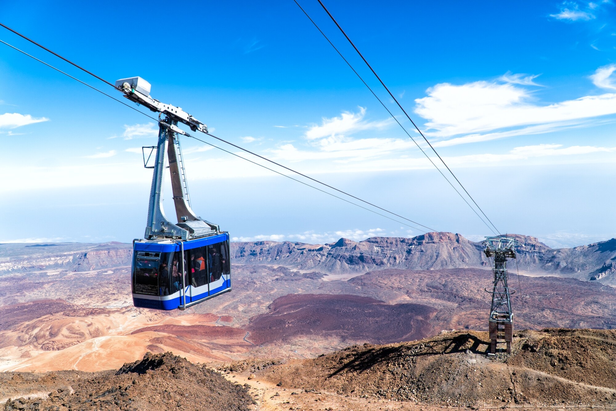 Eine Seilbahn vor karger hügeliger Landschaft, im Hintergrund das Meer. Eine Seilbahn vor karger hügeliger Landschaft, im Hintergrund das Meer.