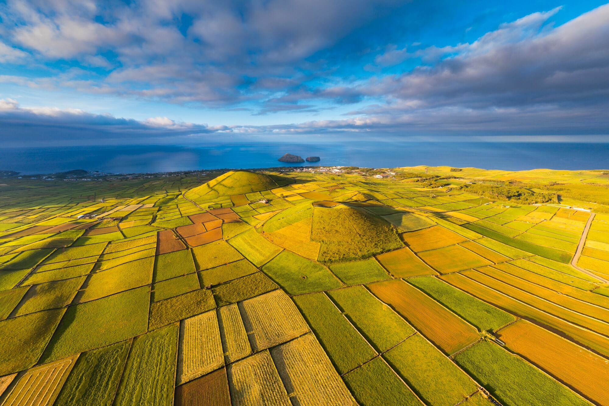 Grünes Landschaftspanorama mit landwirtschaftlichen Parzellen auf Vulkankratern am Meer.