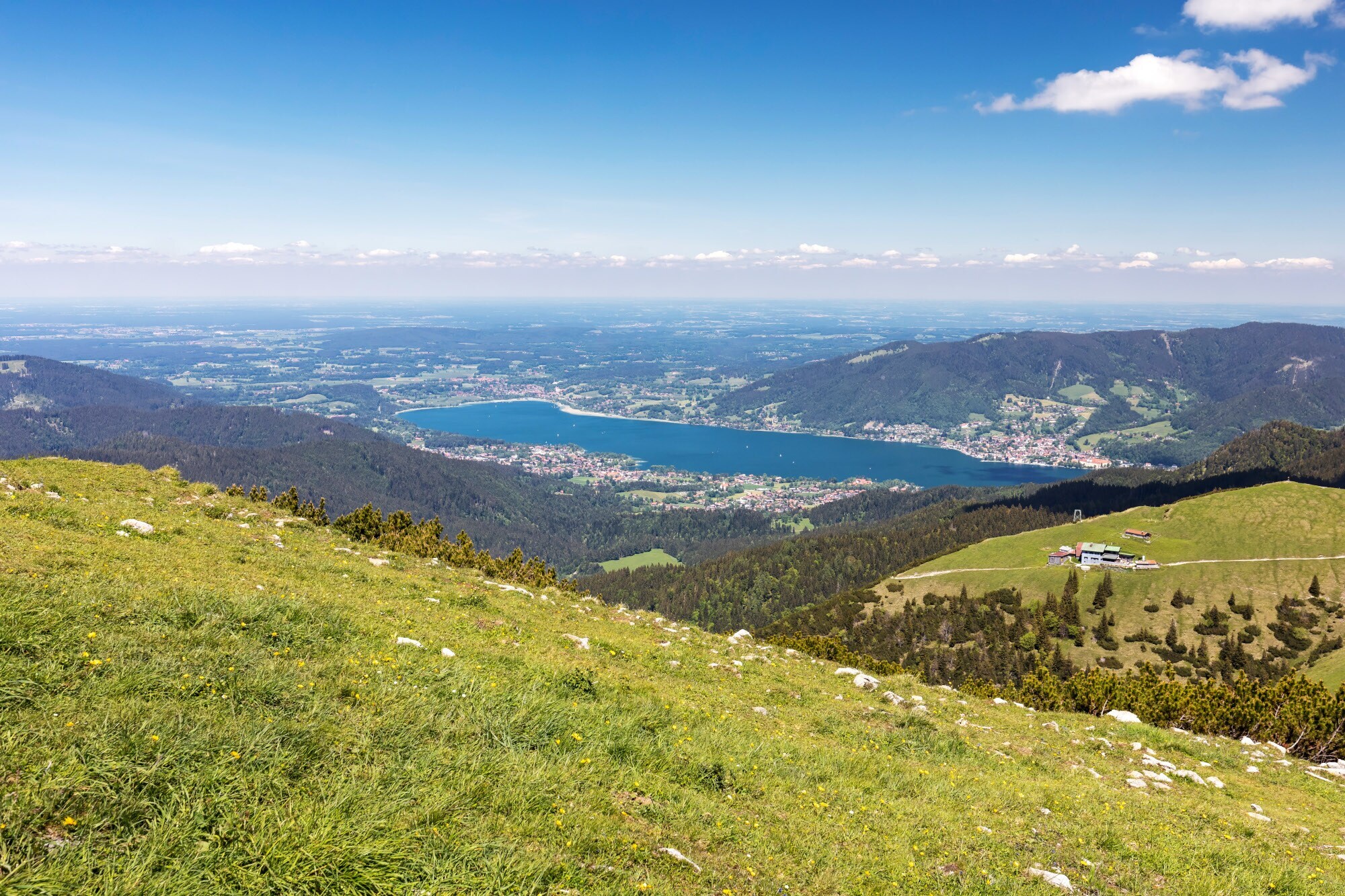 Panoramablick auf den Tegernsee von einer grasbewachsenen Bergkuppe aus.