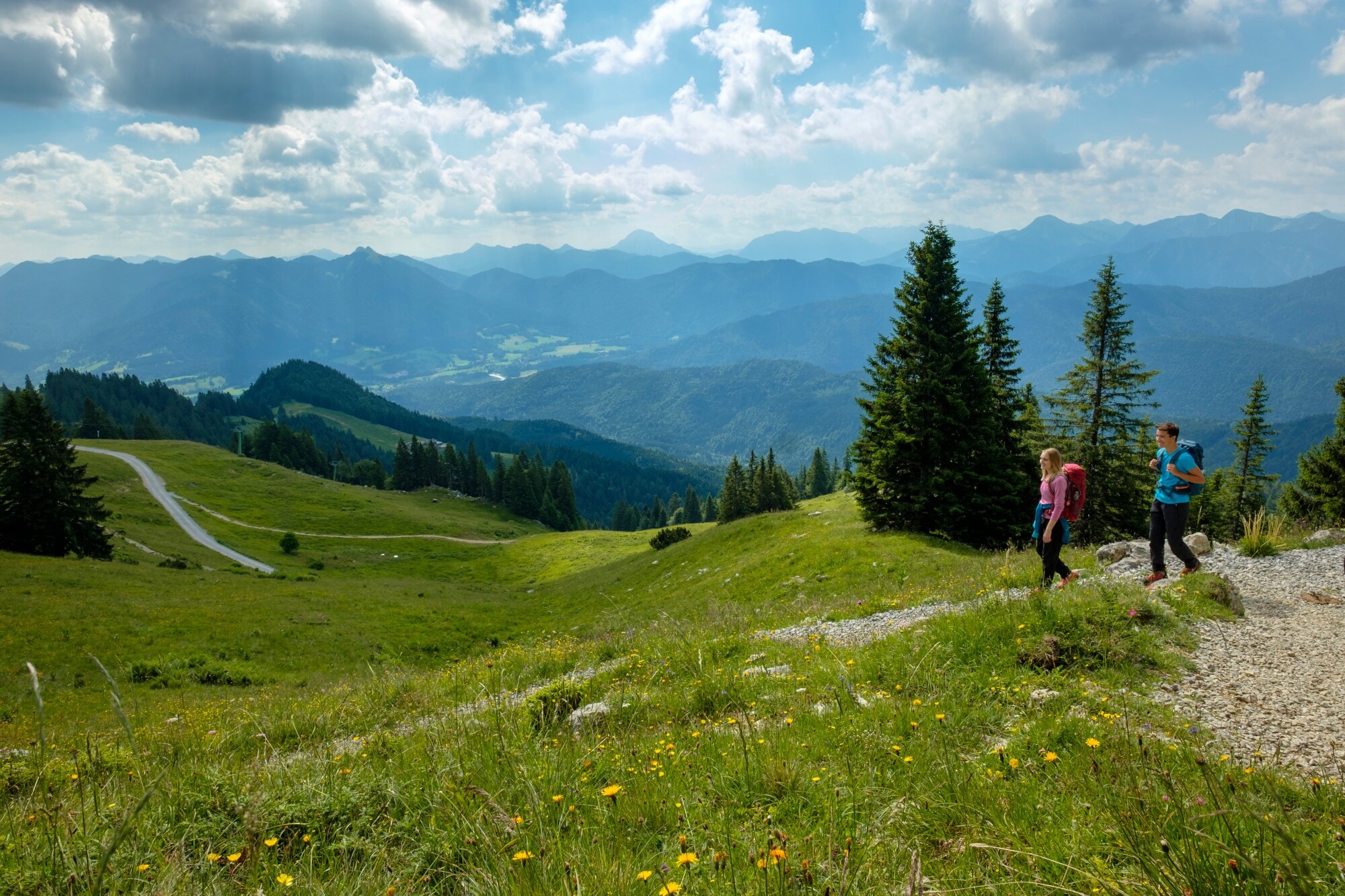 Ein wanderndes Paar mit Rucksäcken auf einem Weg inmitten einer grünen Berglandschaft. Ein wanderndes Paar mit Rucksäcken auf einem Weg inmitten einer grünen Berglandschaft.