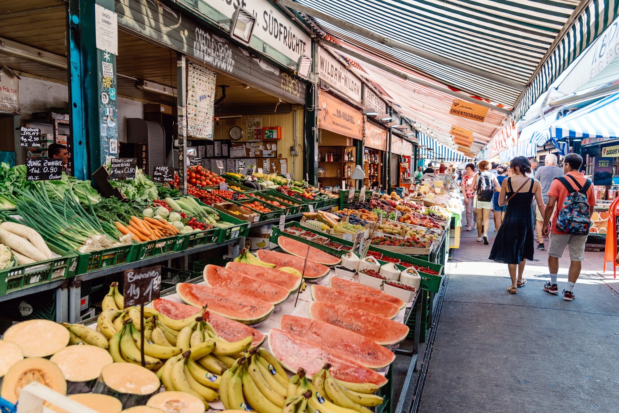 Personen auf einer Marktstraße mit Obst- und Gemüseauslagen. Personen auf einer Marktstraße mit Obst- und Gemüseauslagen.