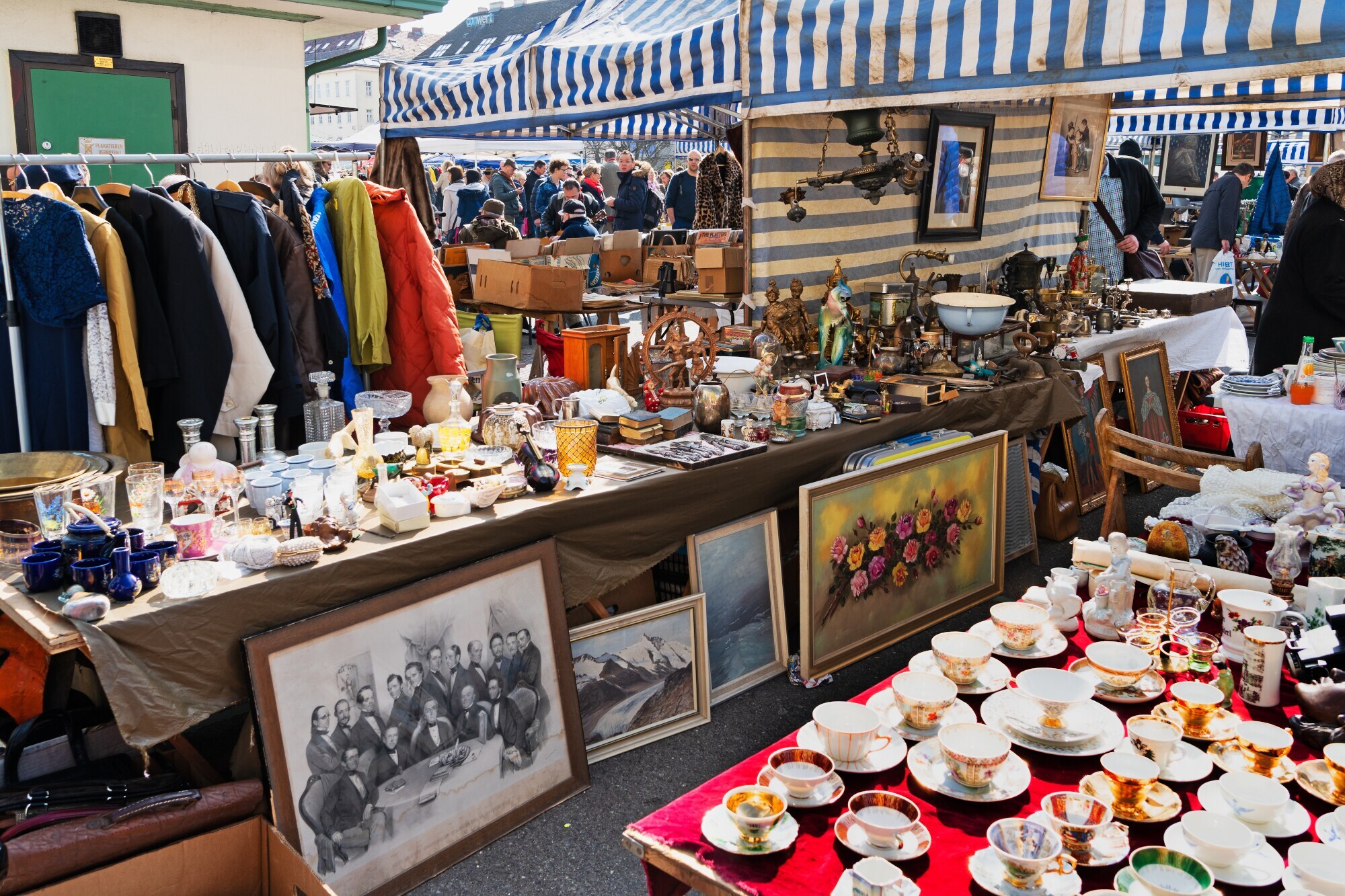 Stände mit Antiquitäten auf einem Trödelmarkt, im Hintergrund Personen.