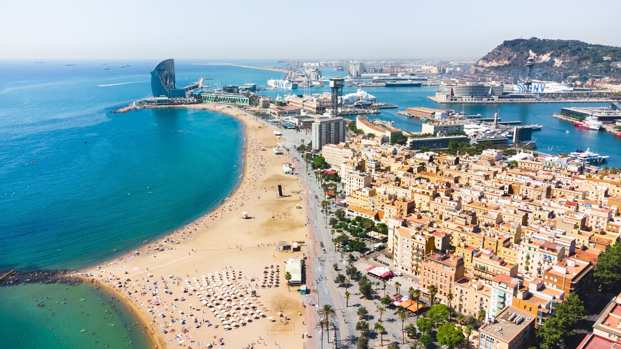 Luftaufnahme eines Stadtteils zwischen Strand und Hafen auf einer Landzunge in Barcelona.