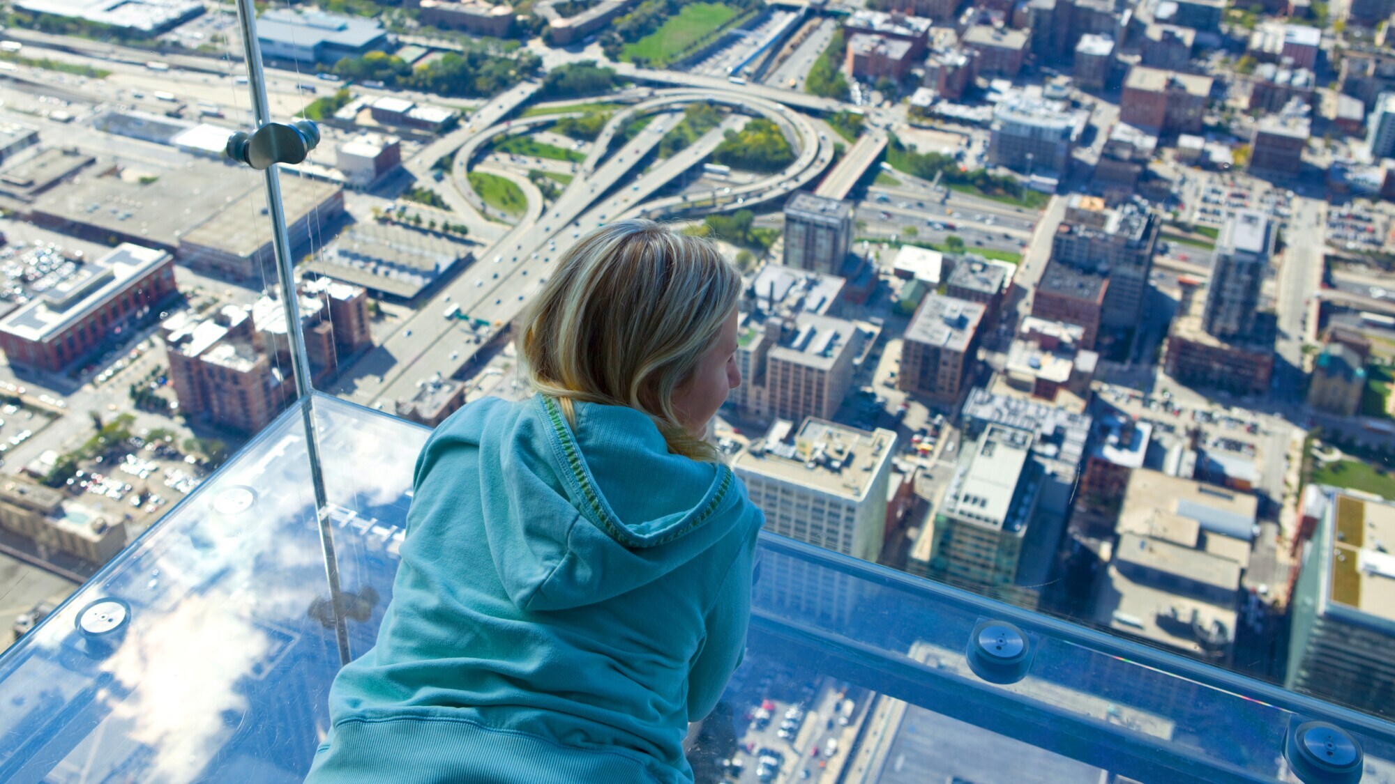 Aufsicht einer auf einem Glasbalkon liegenden Frau über der Skyline Chicagos aus der Vogelperspektive.