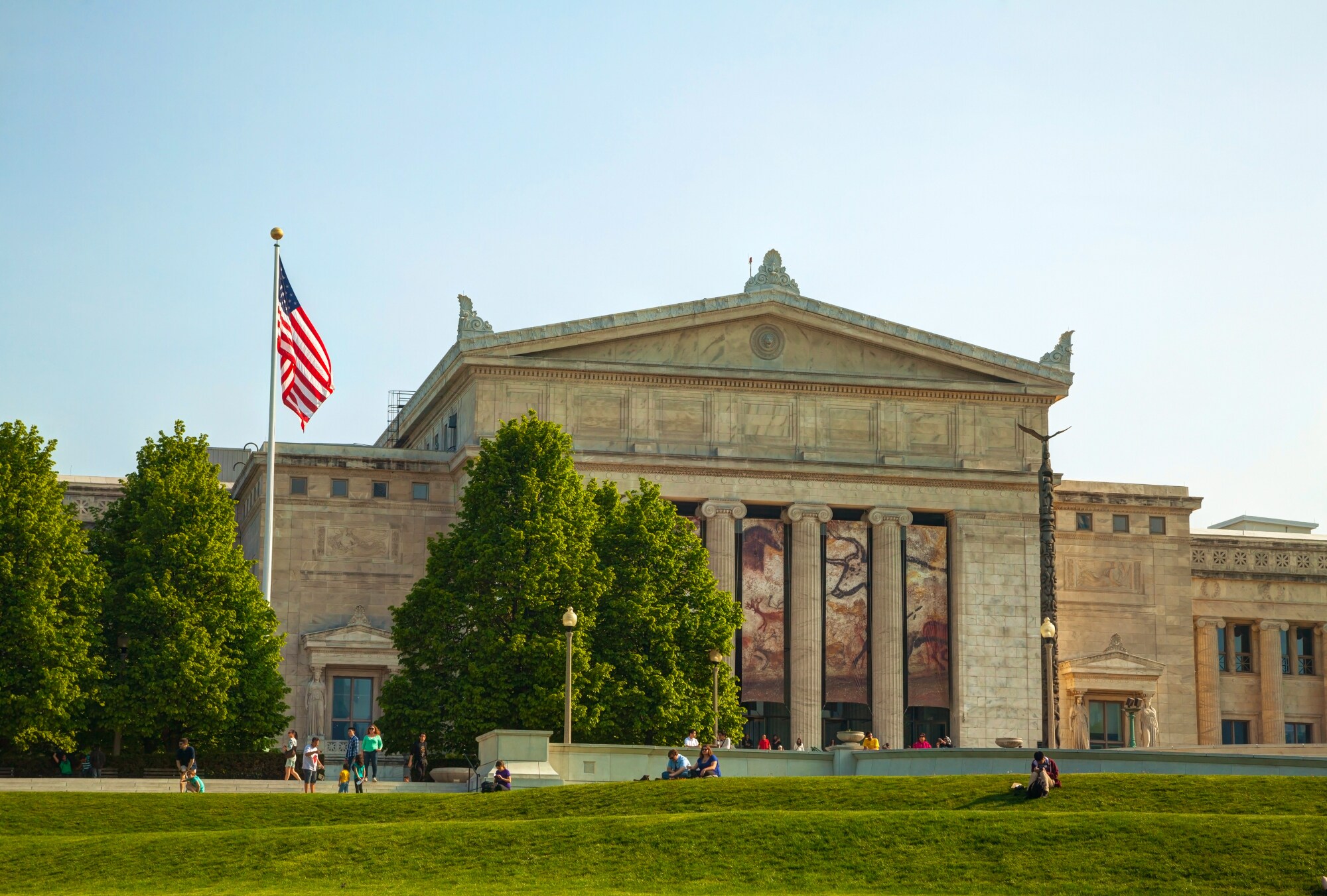 Imposantes Museumsgebäude im neoklassizistischen Baustil, davor eine wehende US-amerikanische Flagge und Personen auf einer Wiese. Imposantes Museumsgebäude im neoklassizistischen Baustil, davor eine wehende US-amerikanische Flagge und Personen auf einer Wiese.