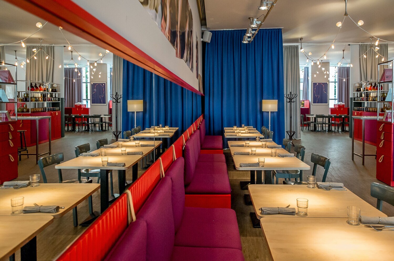 Modernes Restaurant mit hellen Holztischen und roten Sitzbänken an einer Spiegelwand.