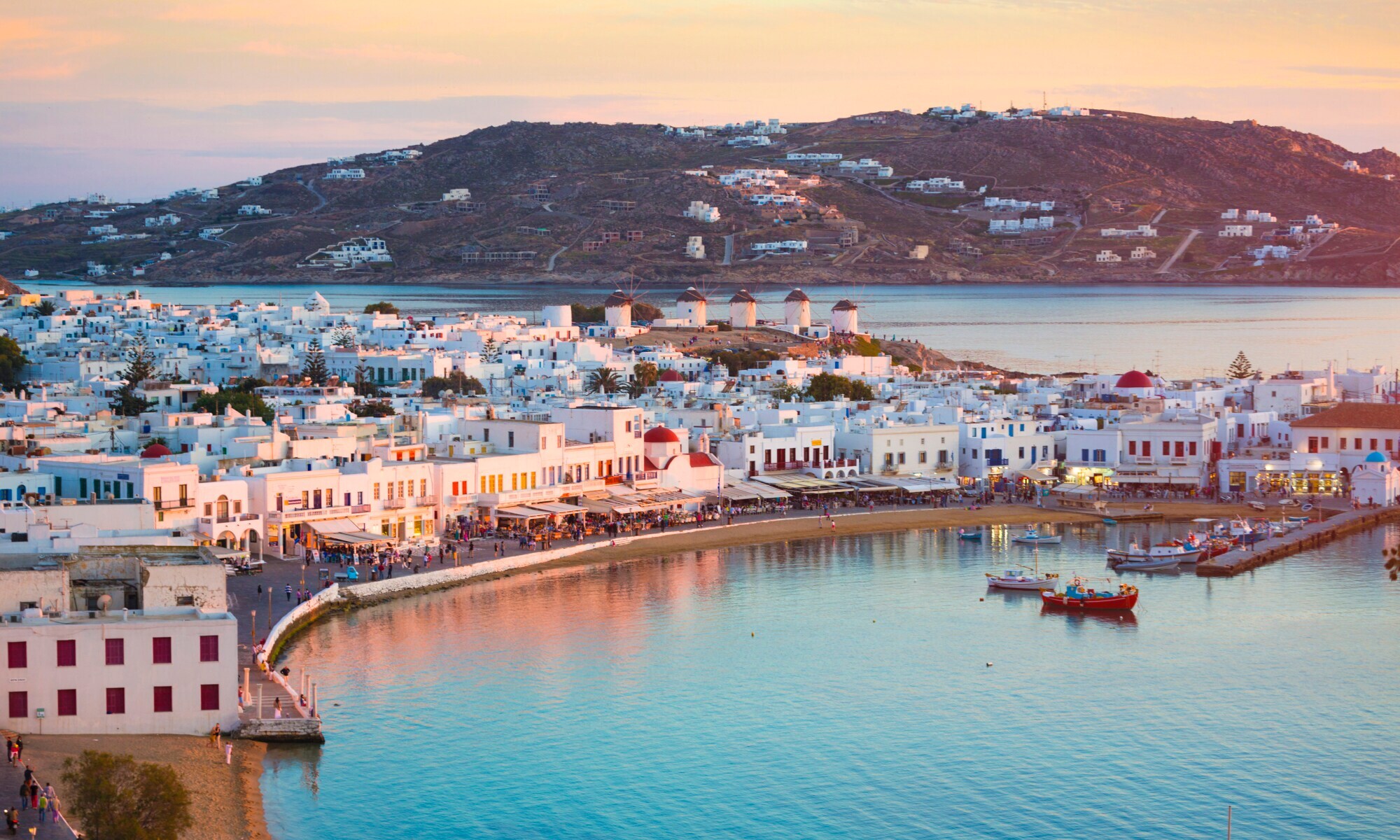 Mykonos-Stadt mit weißen Häusern und belebter Uferpromenade bei Abenddämmerung.
