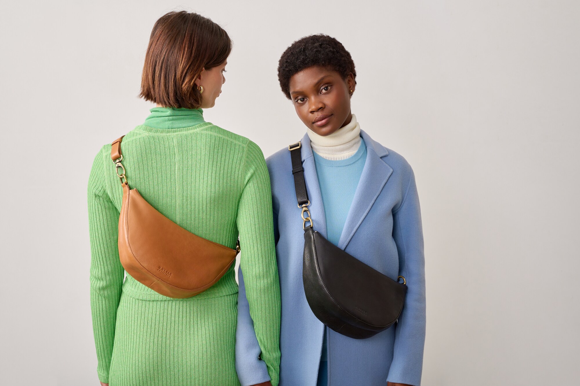 Zwei weibliche Models mit halbmondförmigen Umhängetaschen aus Leder. Zwei weibliche Models mit halbmondförmigen Umhängetaschen aus Leder.