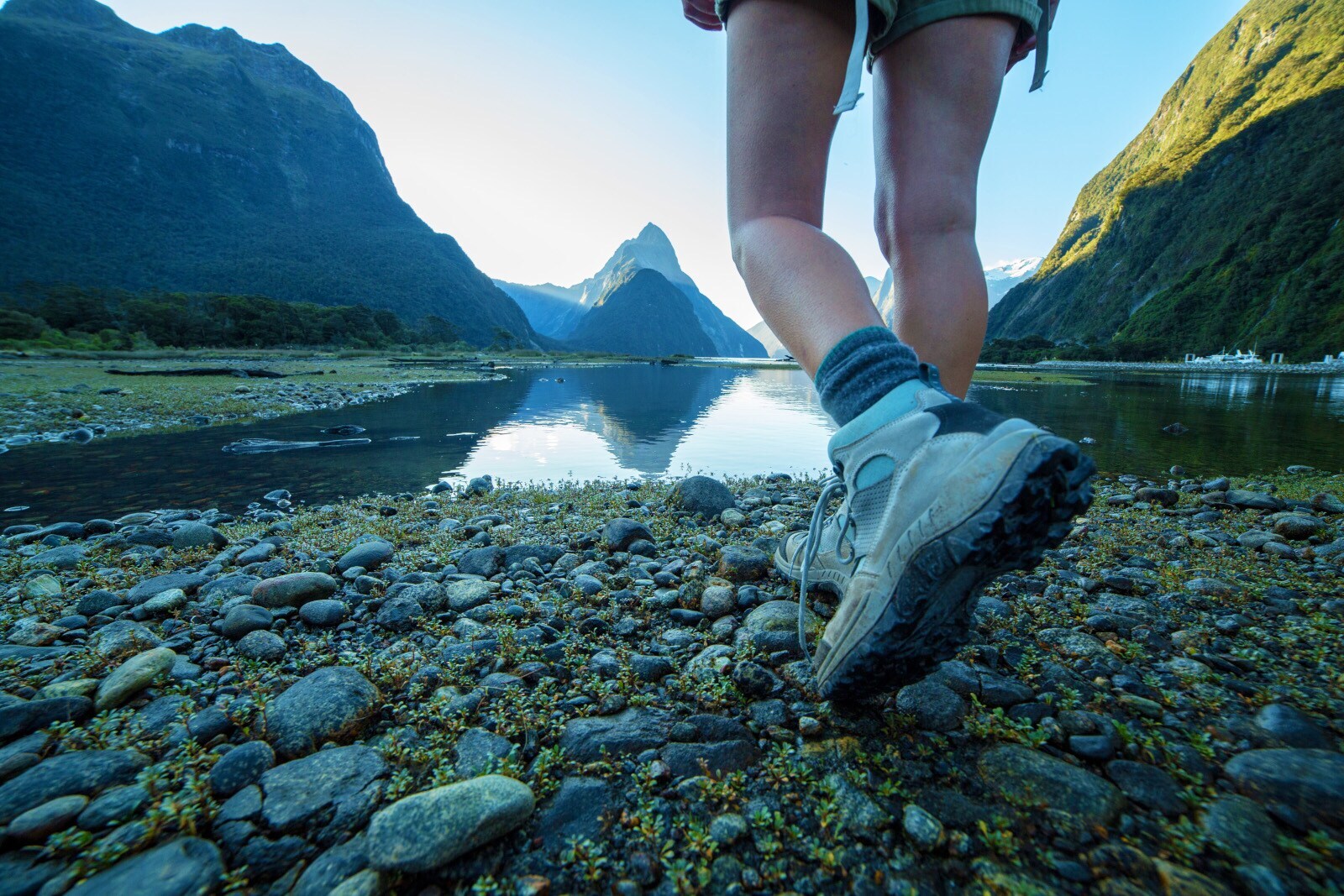 Zwei Beine einer Person in Wanderschuhen an einem See vor Bergpanorama. Zwei Beine einer Person in Wanderschuhen an einem See vor Bergpanorama.