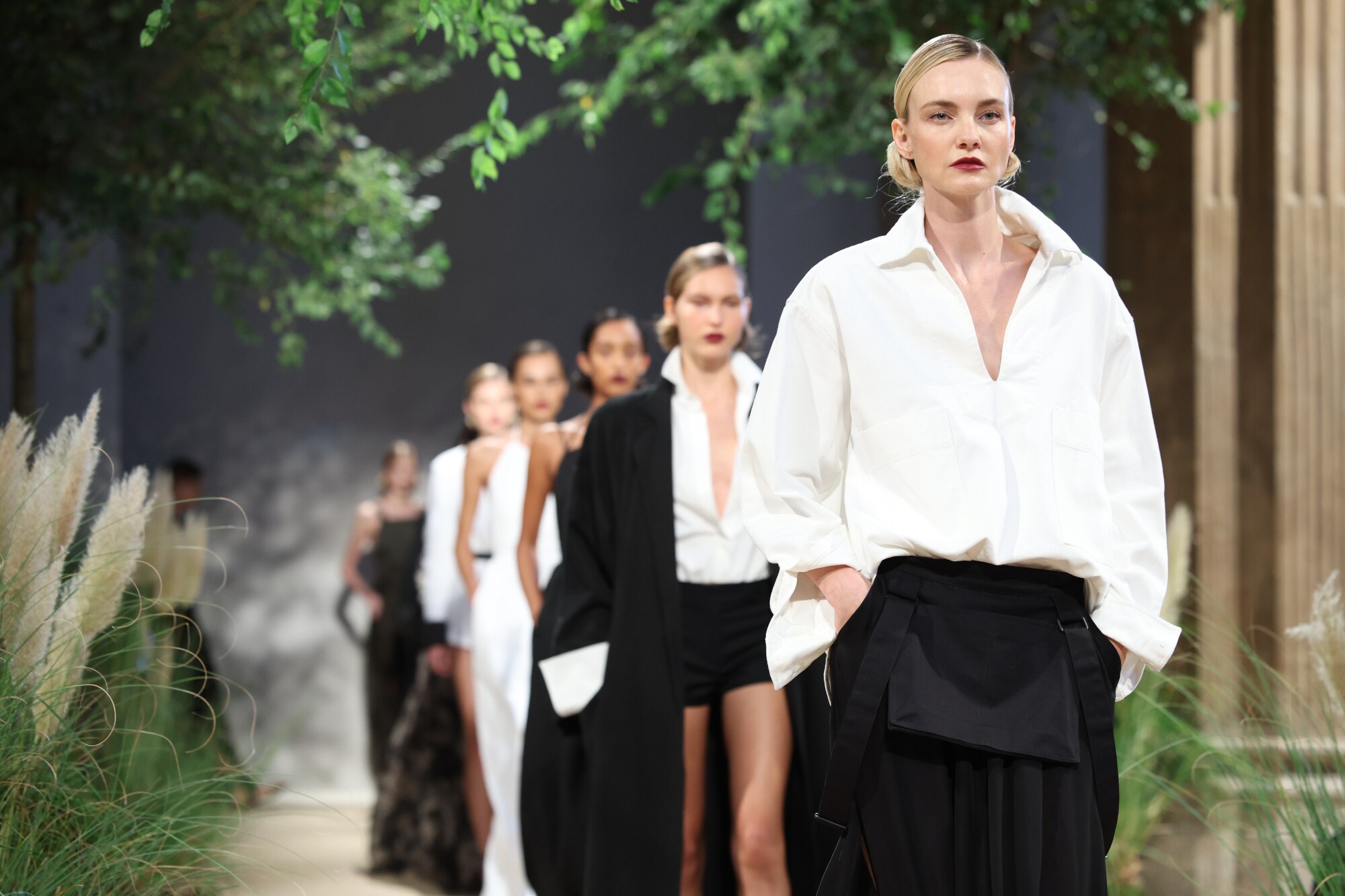 Weibliche Models in eleganter Kleidung mit klassischen Schnitten in den Farben Schwarz und Weiß auf einem Laufsteg bei einer Modenschau.