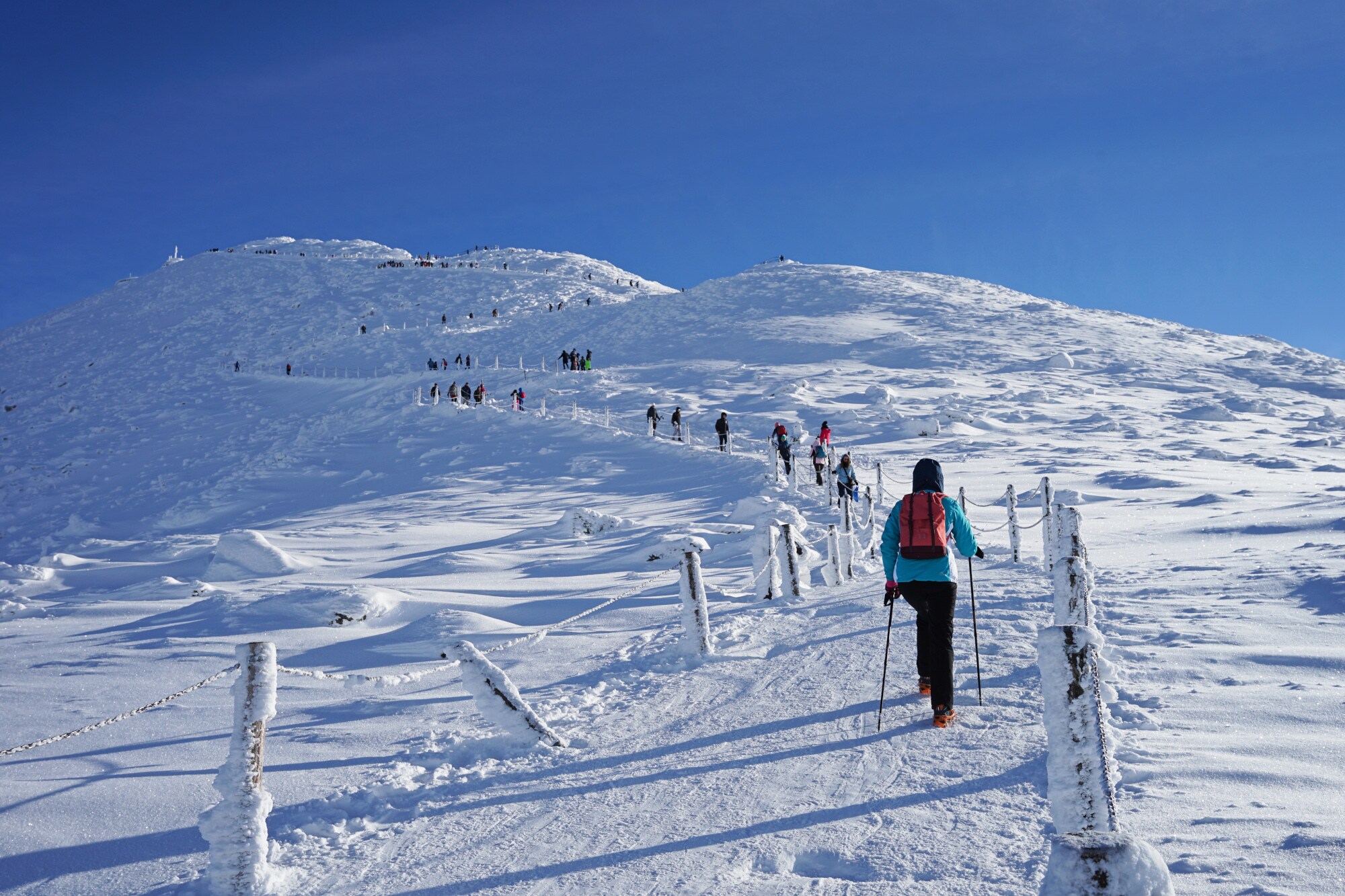 Personen wandern auf einem Weg einen schneebedeckten Hügel hinauf.