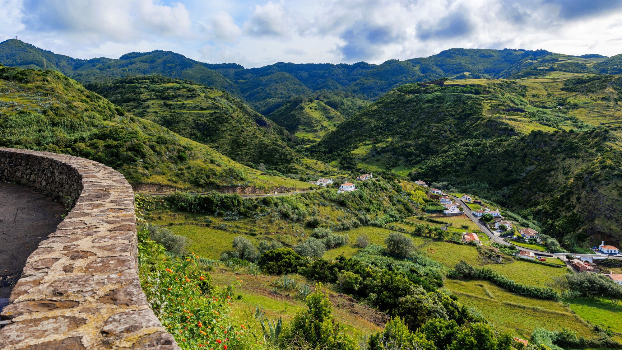 Blick von einer Mauer auf eine saftig grüne Hügellandschaft mit kleiner Ortschaft.