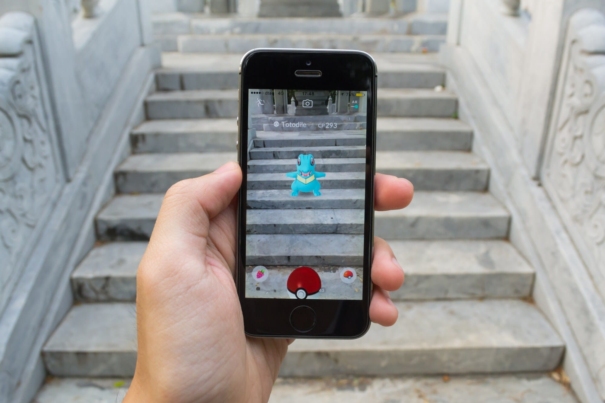 Ein in der Hand gehaltenes Smartphone mit einem blauen Monster in der Pokémon Go AR-App auf dem Display. Ein in der Hand gehaltenes Smartphone mit einem blauen Monster in der Pokémon Go AR-App auf dem Display.