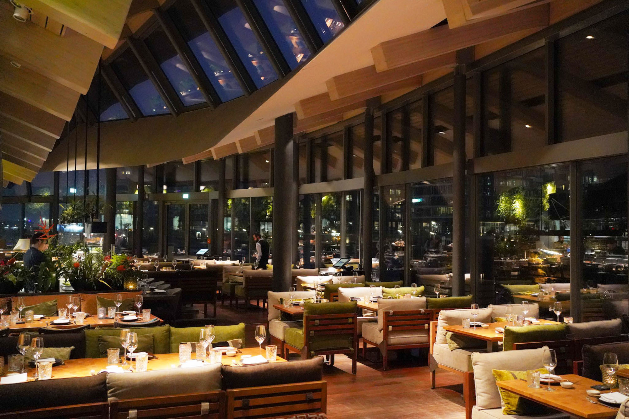 Speiseraum eines modernen Restaurants mit geschwungenem Dach und umlaufender Glasfassade bei Nacht.