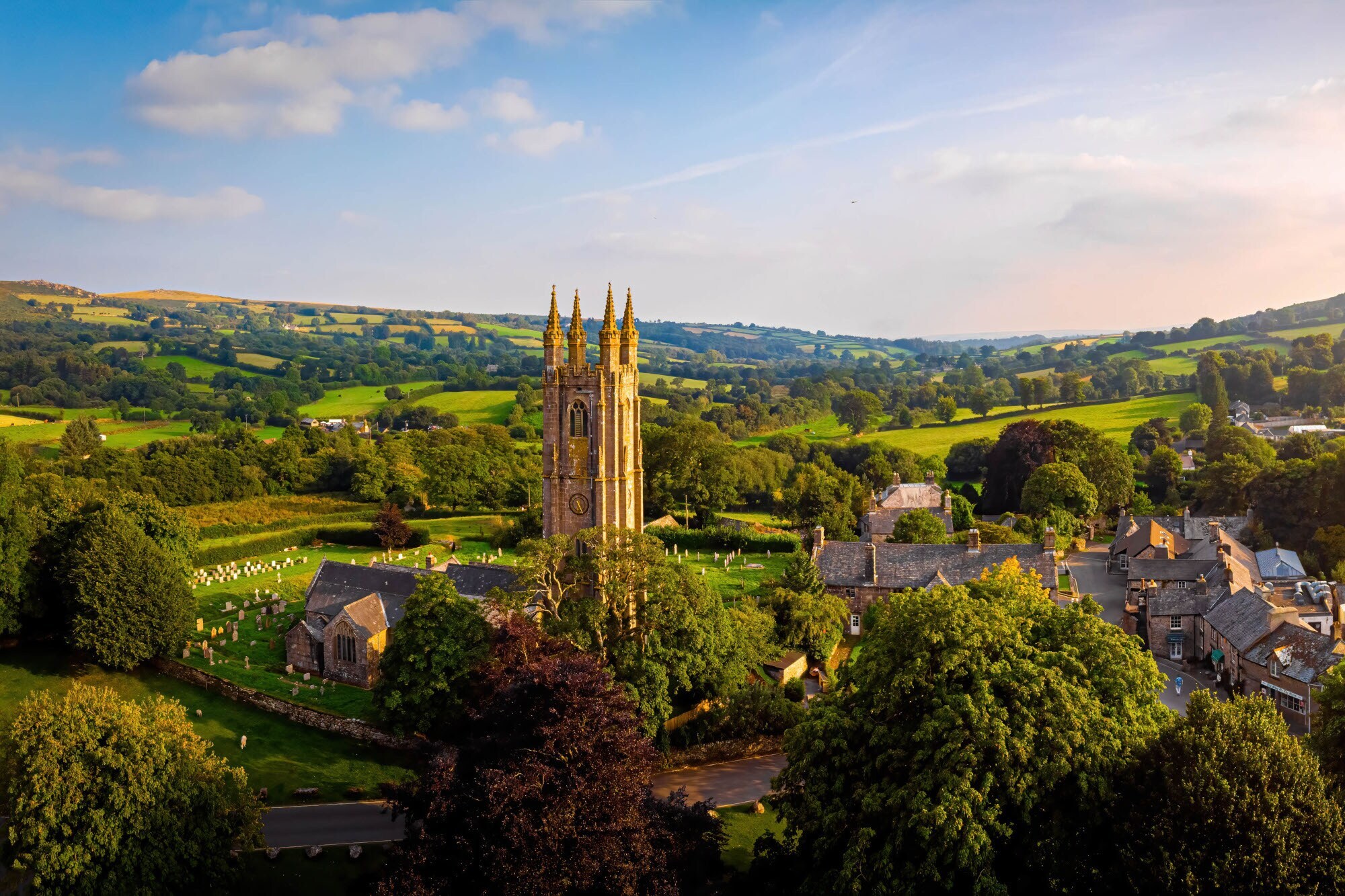 Kleine Ortschaft mit Steinhäusern und Kirche im anglo-normannischen Stil, umgeben von Schafen, inmitten einer grünen Hügellandschaft.
