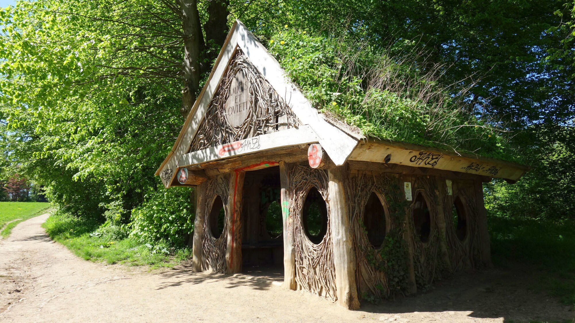Eine Holzhütte mit einem grasbewachsenen Dach und ovalen Fenstern in einem Park.