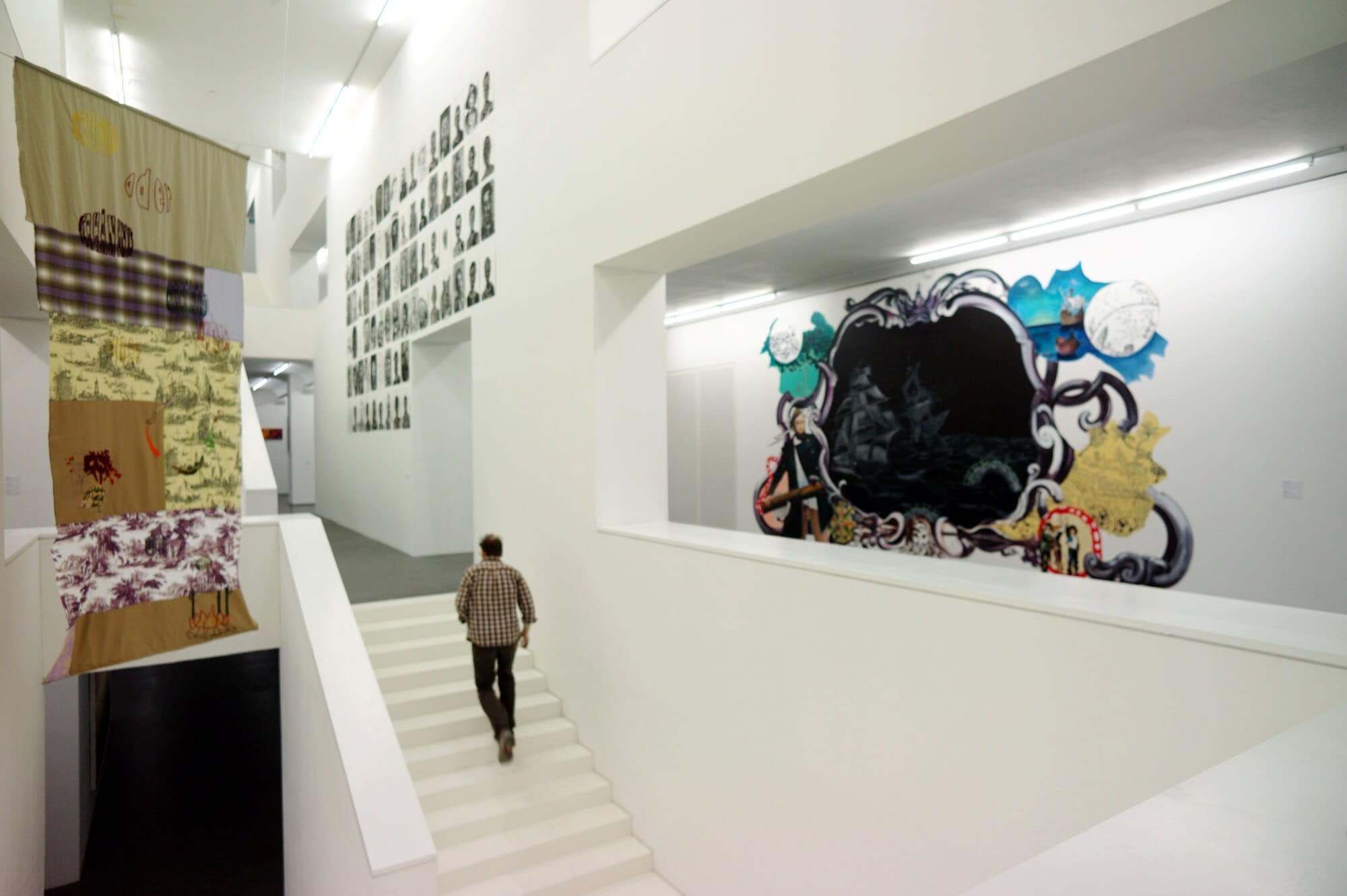 Eine Person läuft in einem Museum mit moderner Kunst eine weiße Treppe hinauf. Eine Person läuft in einem Museum mit moderner Kunst eine weiße Treppe hinauf.