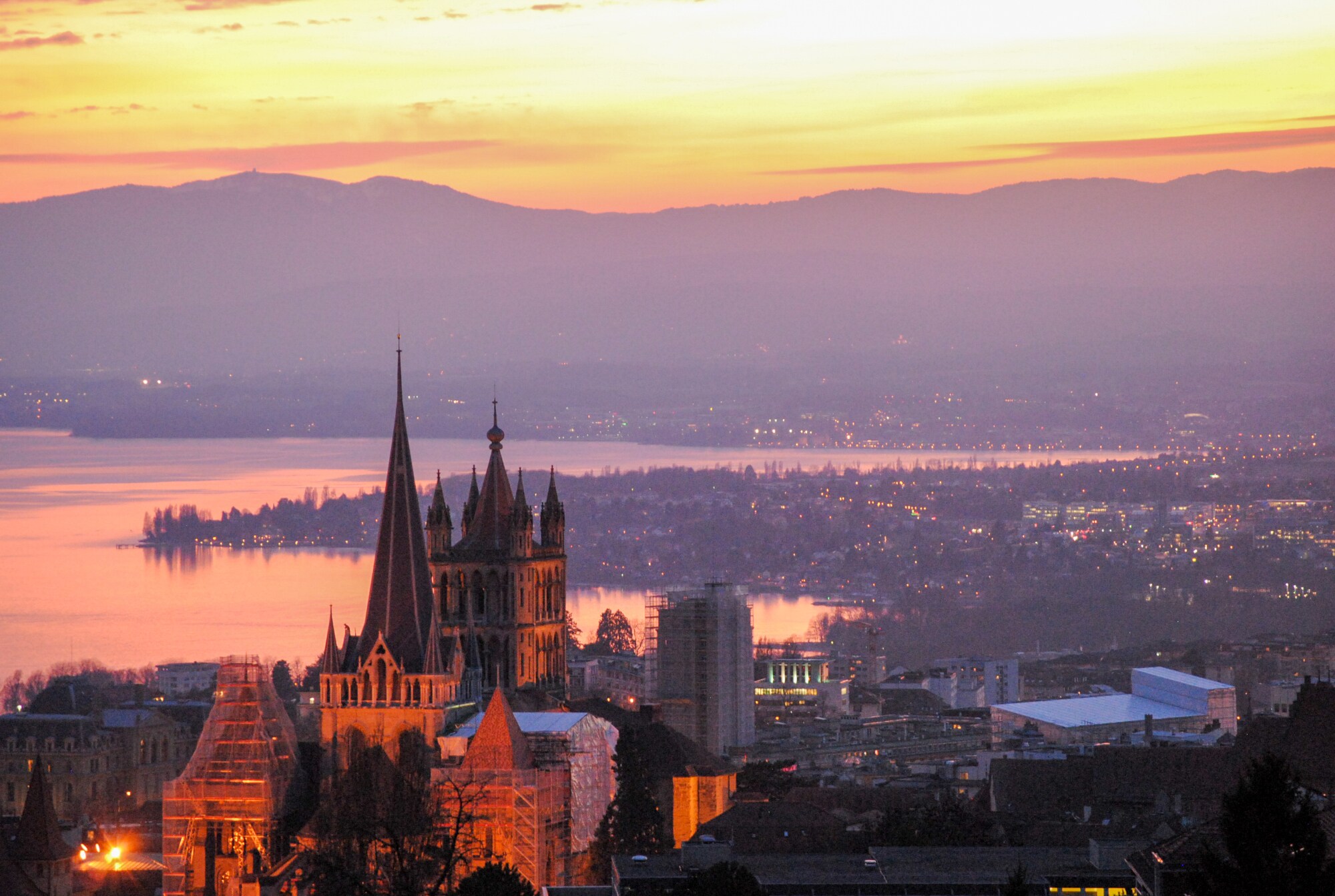 Luftaufnahme von Lausanne am Abend, mit Kathedrale Notre-Dame im Vordergrund.