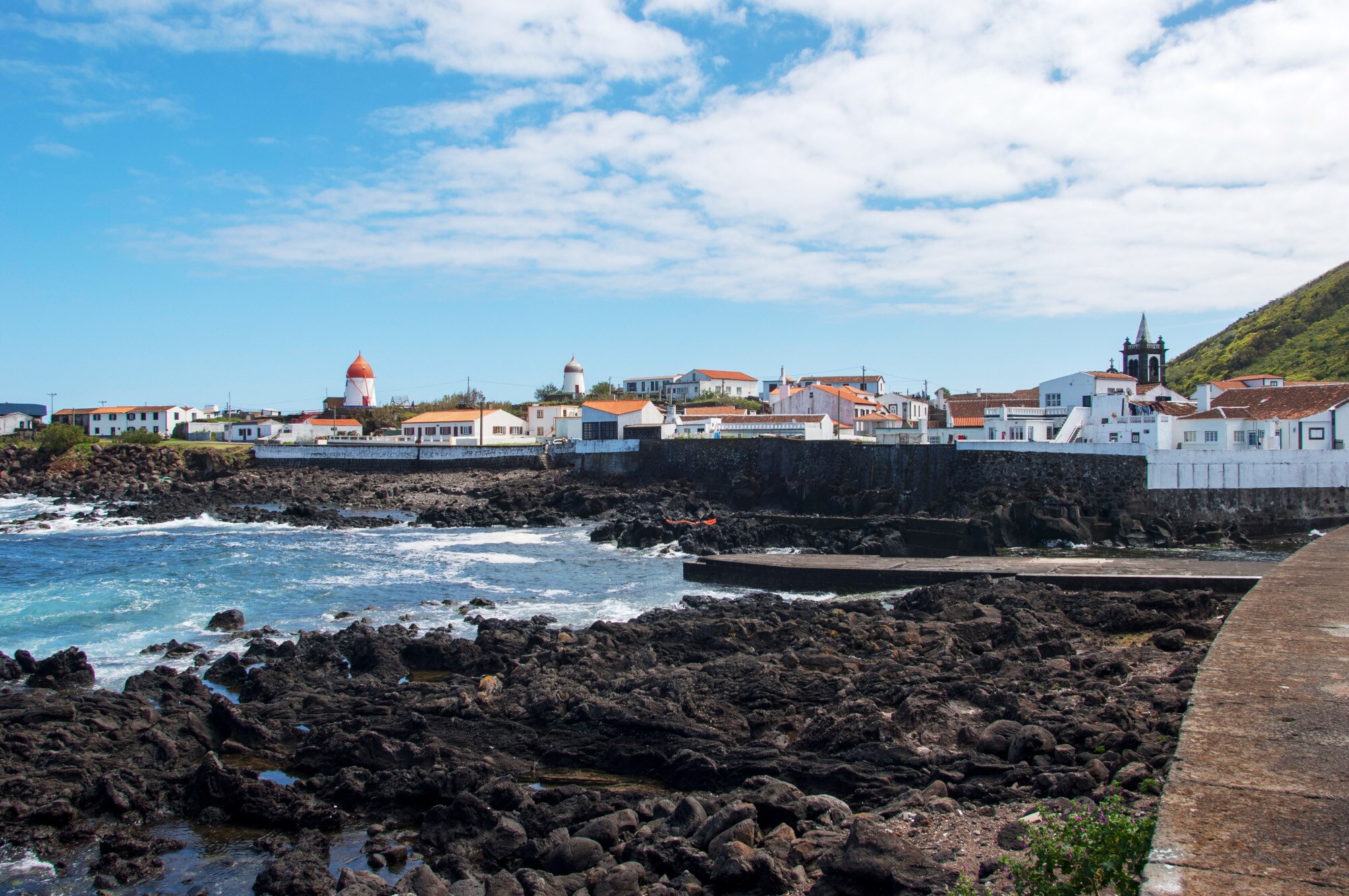Ortschaft mit weißen Häusern hinter einem Strand aus schwarzem Lavagestein.