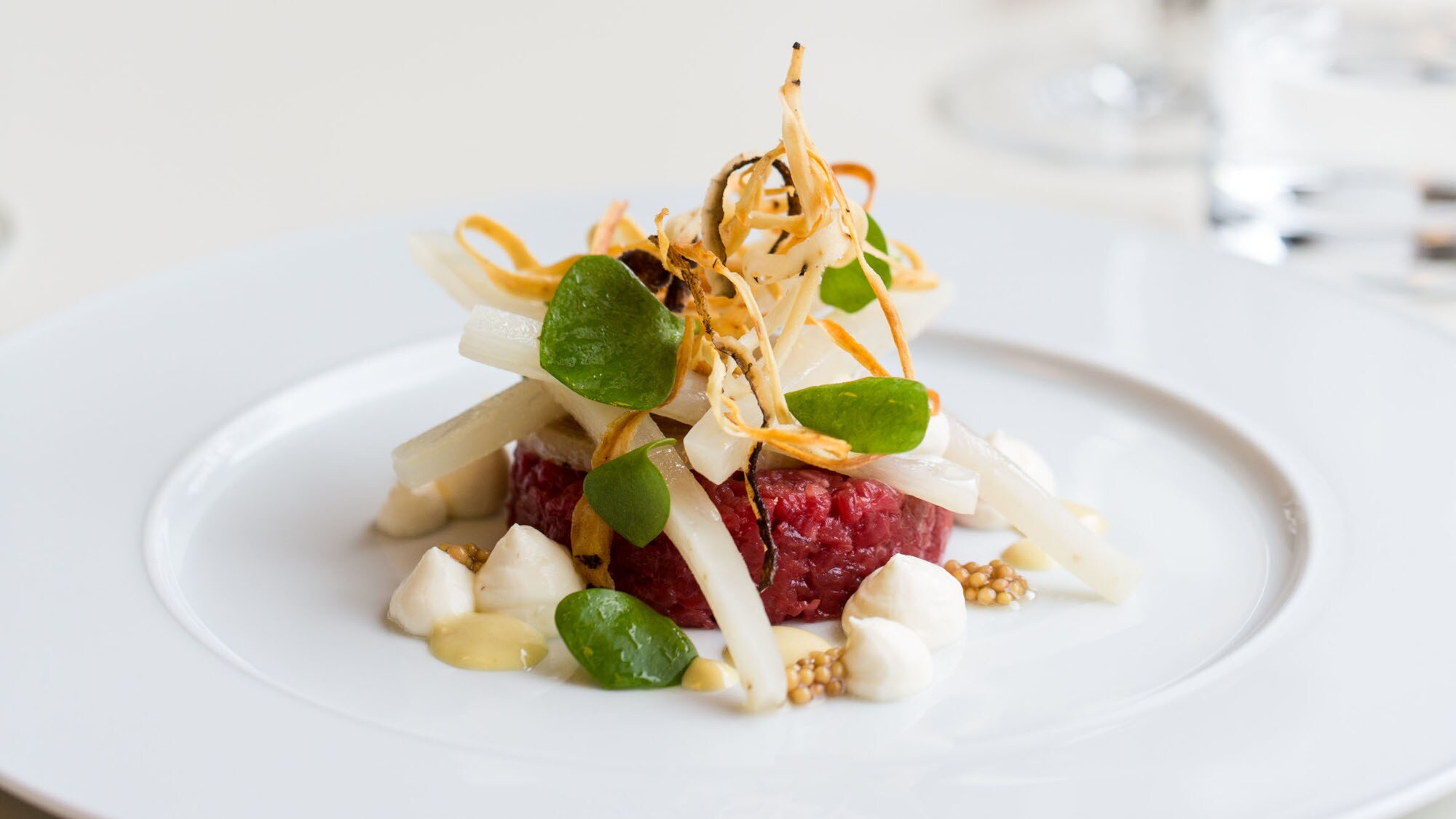 Kunstvoll angerichteter Tatar mit Gemüse auf einem weißen Teller.