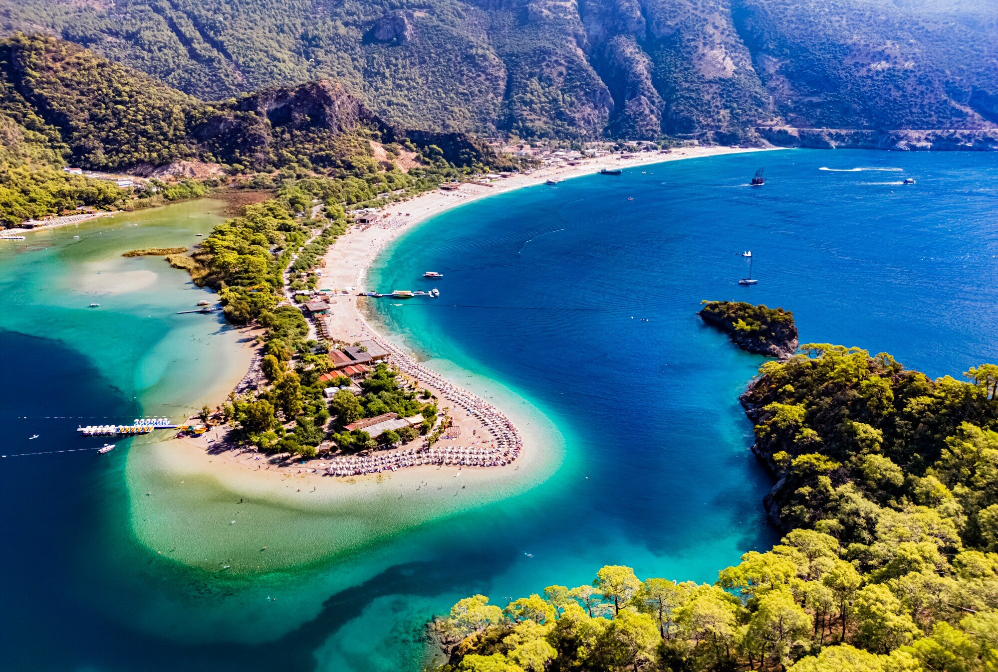 Luftaufnahme einer Landzunge mit weißem Sandstrand und üppiger Begrünung in einer hügeligen Bucht mit azurblauem Wasser. Luftaufnahme einer Landzunge mit weißem Sandstrand und üppiger Begrünung in einer hügeligen Bucht mit azurblauem Wasser.