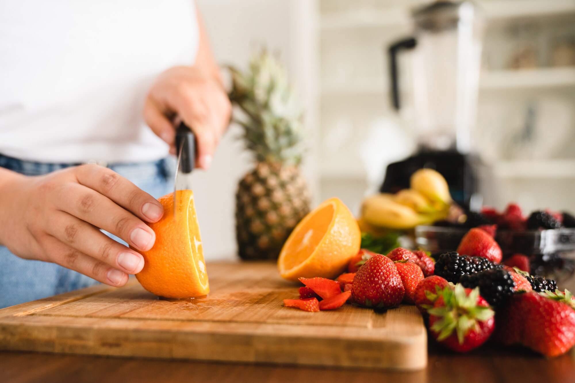 Nahaufnahme von zwei Händen beim Schneiden von Obst auf einem Holzbrett in einer Küche. Nahaufnahme von zwei Händen beim Schneiden von Obst auf einem Holzbrett in einer Küche.