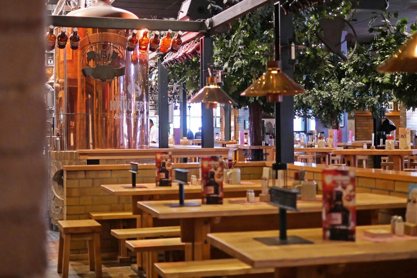 Gastronomiebereich in einem Brauhaus mit Holztischen und großem Kupferkessel.