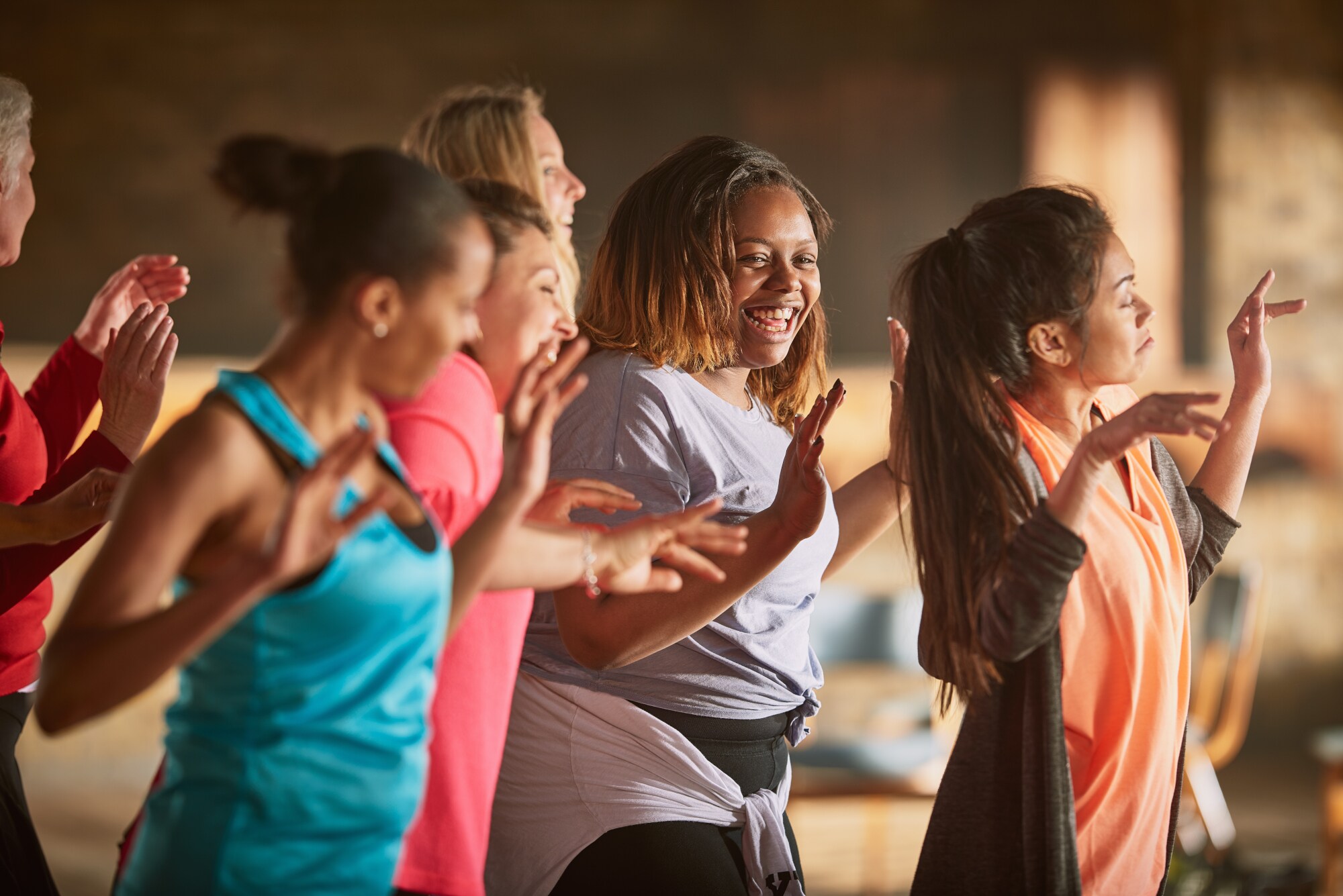 Eine Gruppe Frauen in Sportbekleidung bewegt sich tänzerisch in einem Raum.