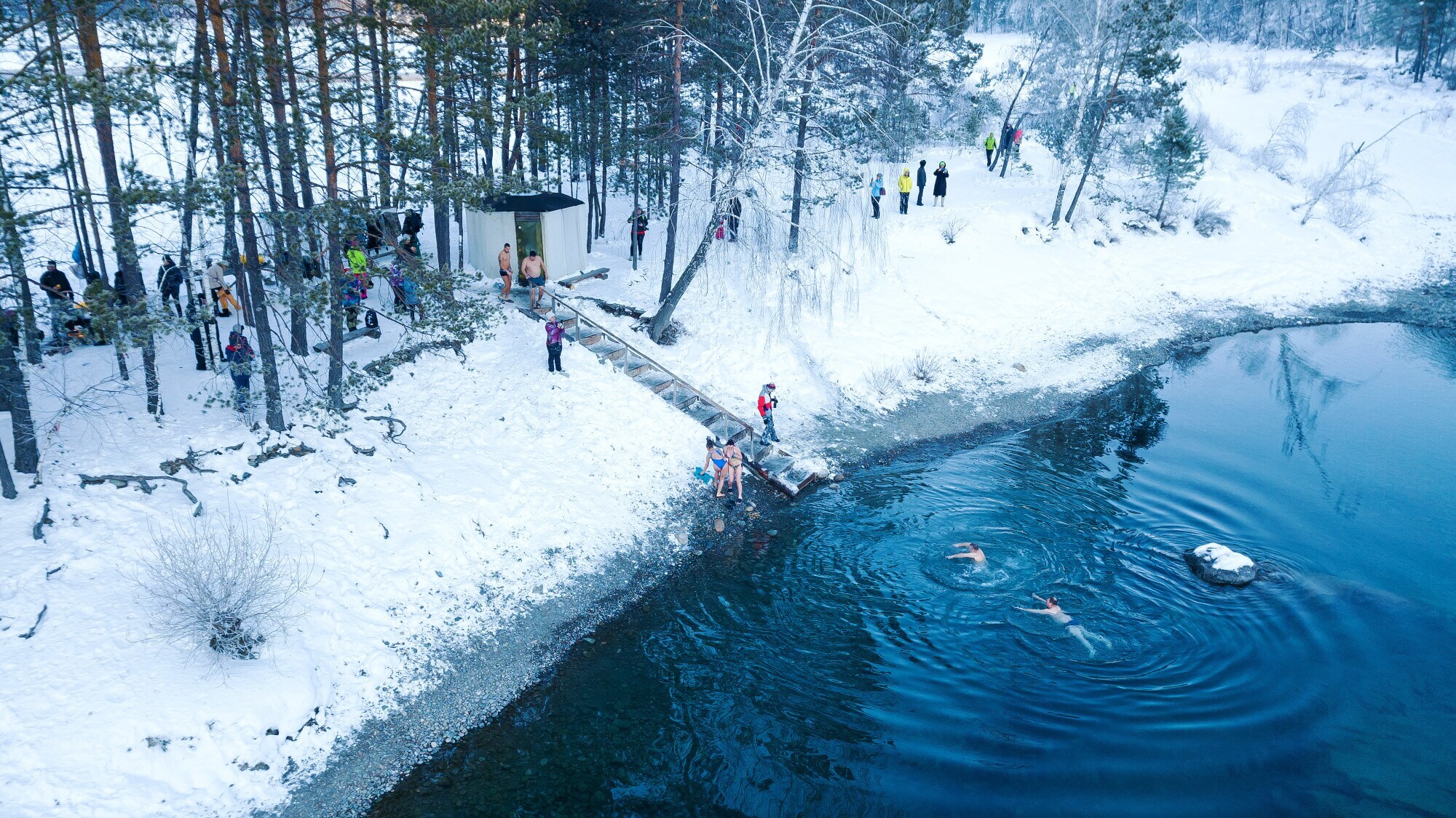 Luftaufnahme von Menschen, die in einem von Schnee umgebenen See baden.