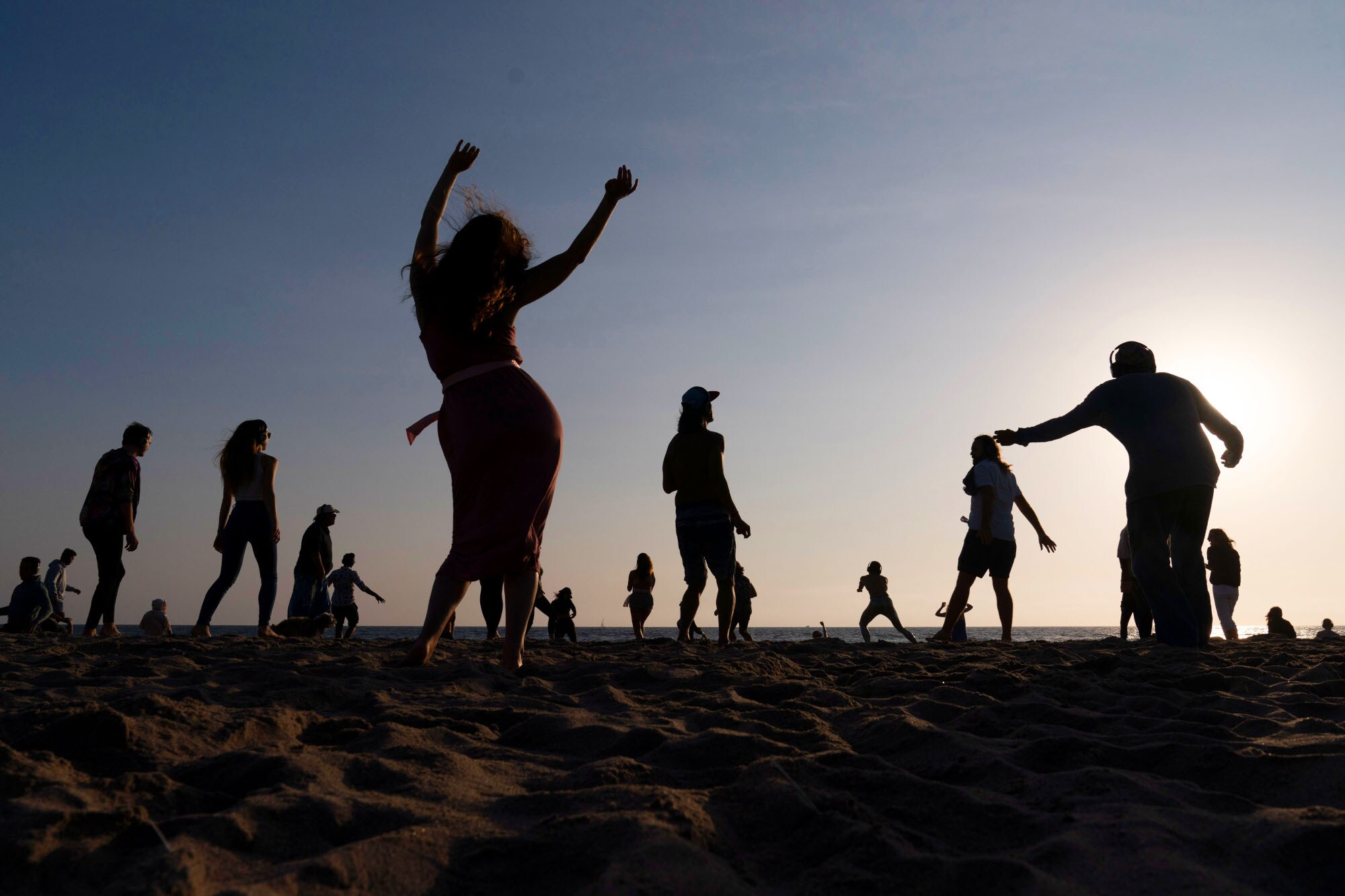 Silhouetten mehrerer tanzender Personen am Strand.