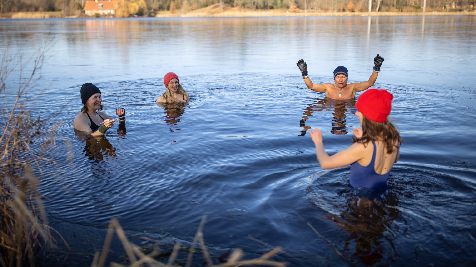 Vier Personen mit Mützen baden in einem See im Winter.